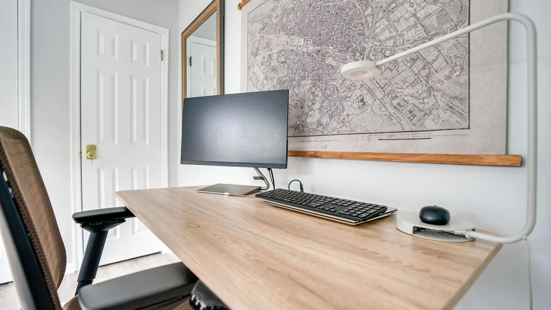Un despacho en casa con escritorio, monitor de computadora y un mapa enmarcado en la pared.