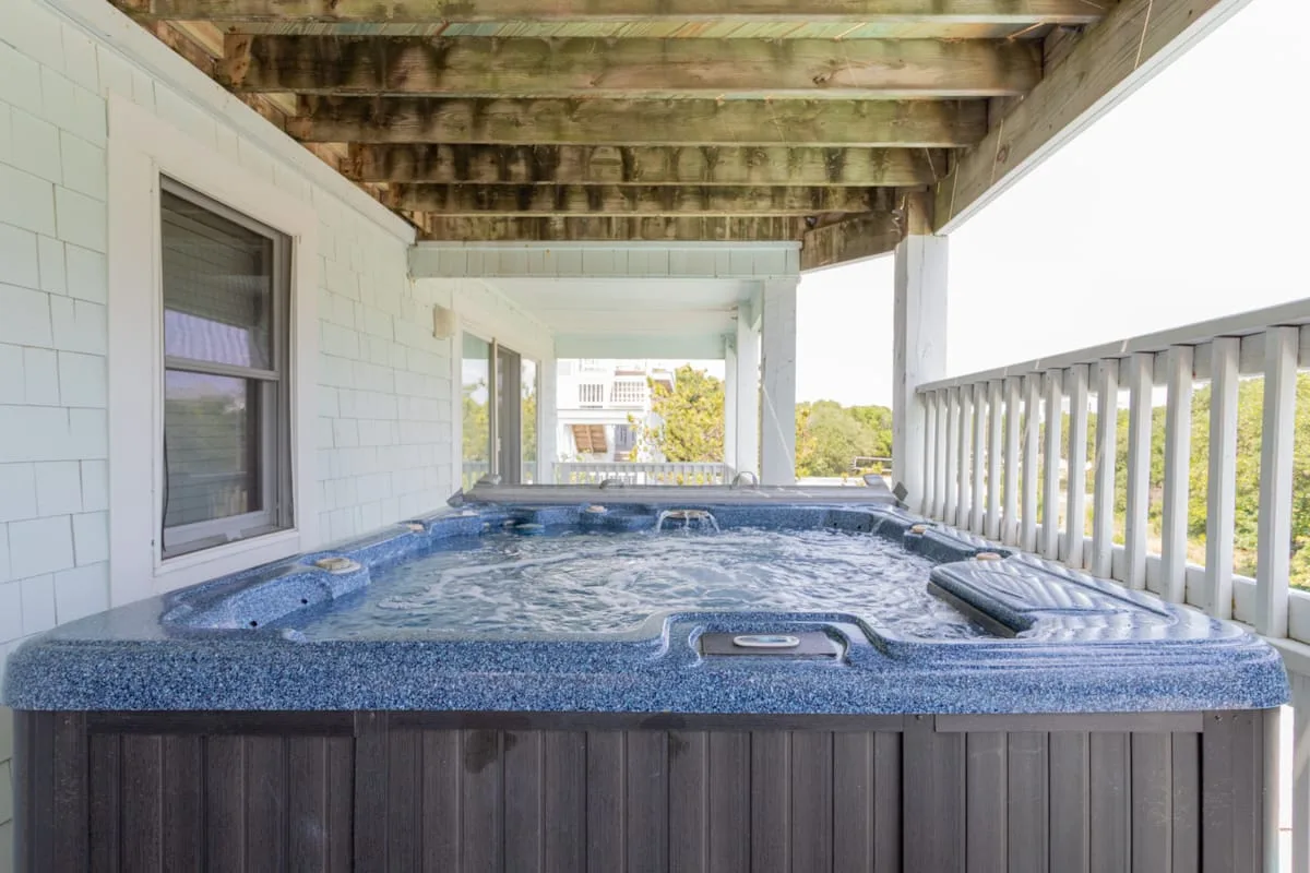A covered outdoor hot tub sits beside a white wall and railing.