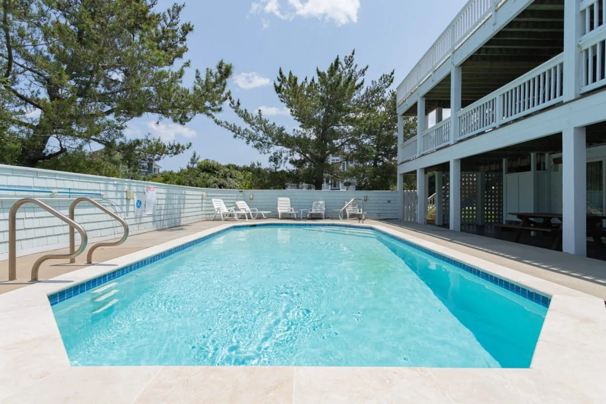 An outdoor swimming pool beside a multi-level building, with trees in the background.