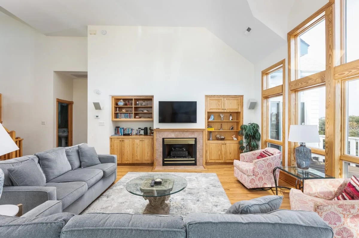 A bright living room with gray seating, a fireplace, and tall windows.