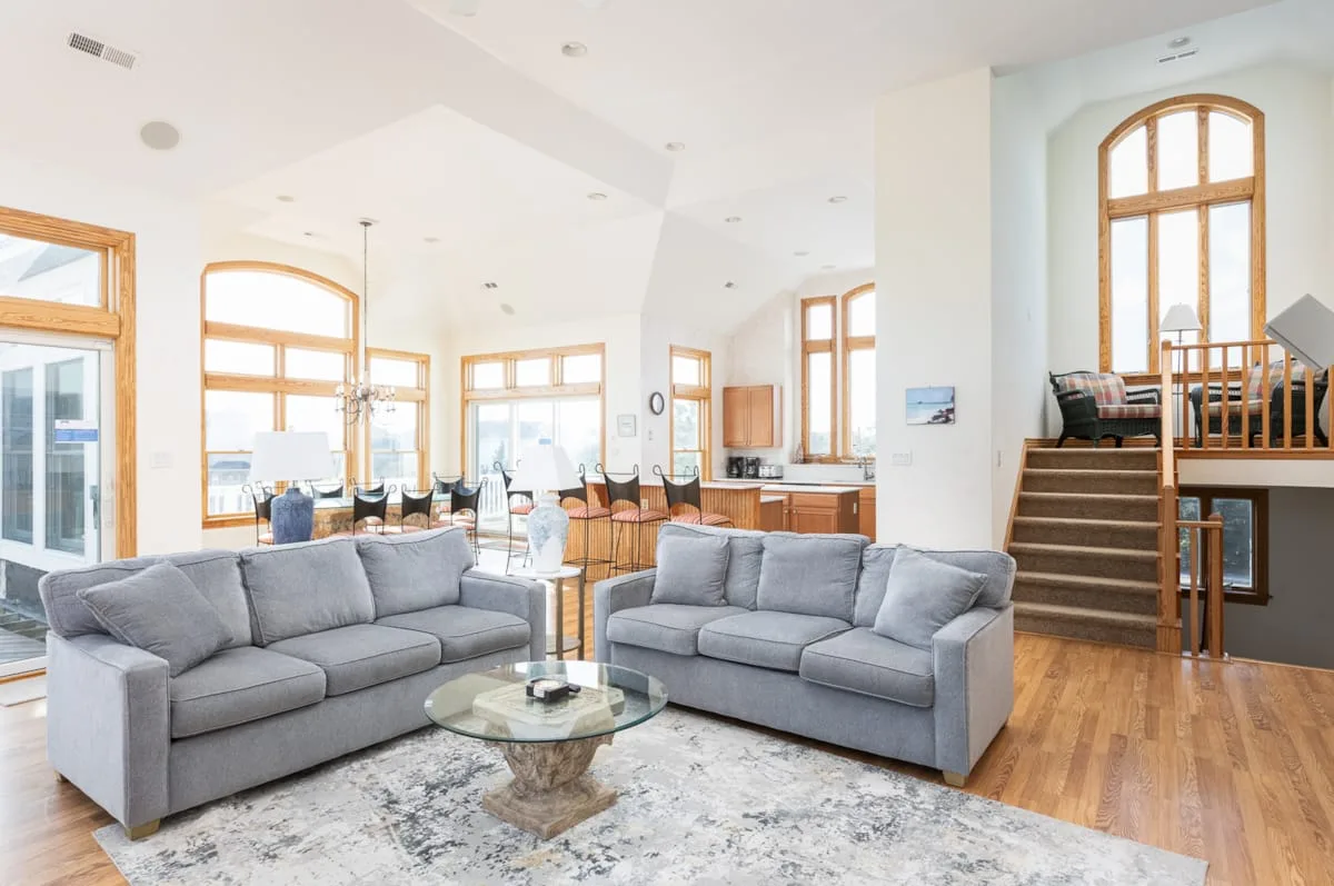 A bright living room with gray seating, large windows, and a staircase.