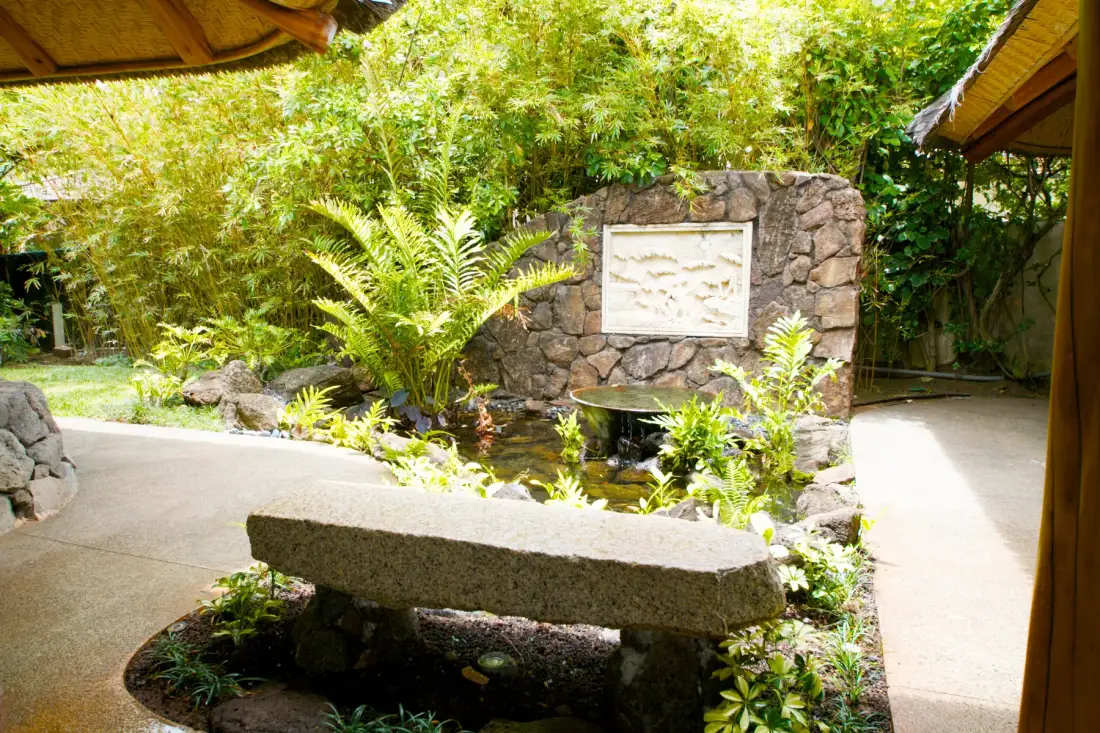 Un patio ajardinado con una fuente de piedra y un banco bajo de piedra.