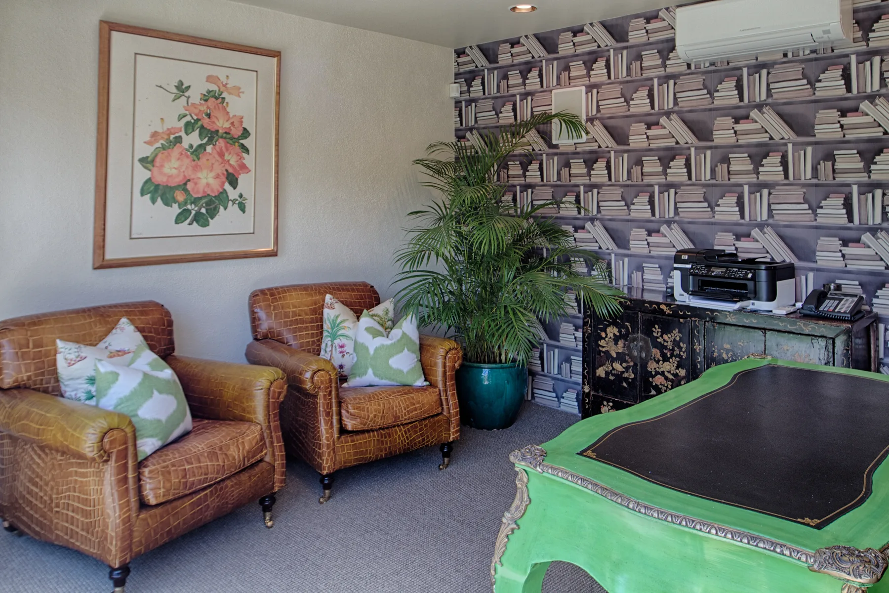 Una sala de estar con sillones estampados, papel tapiz de libros y una mesa verde.