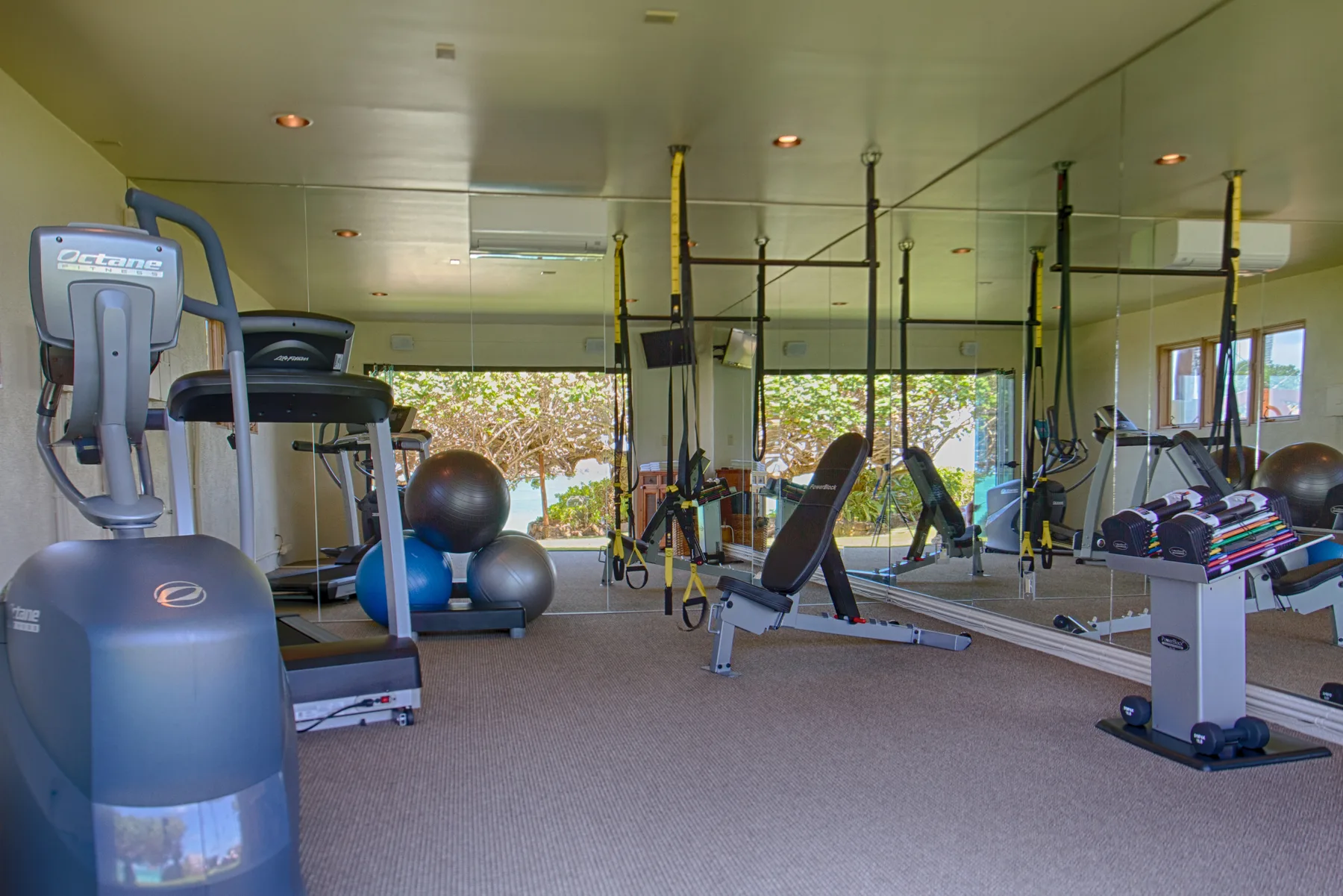 Un gimnasio con equipos de ejercicio y paredes con espejos.