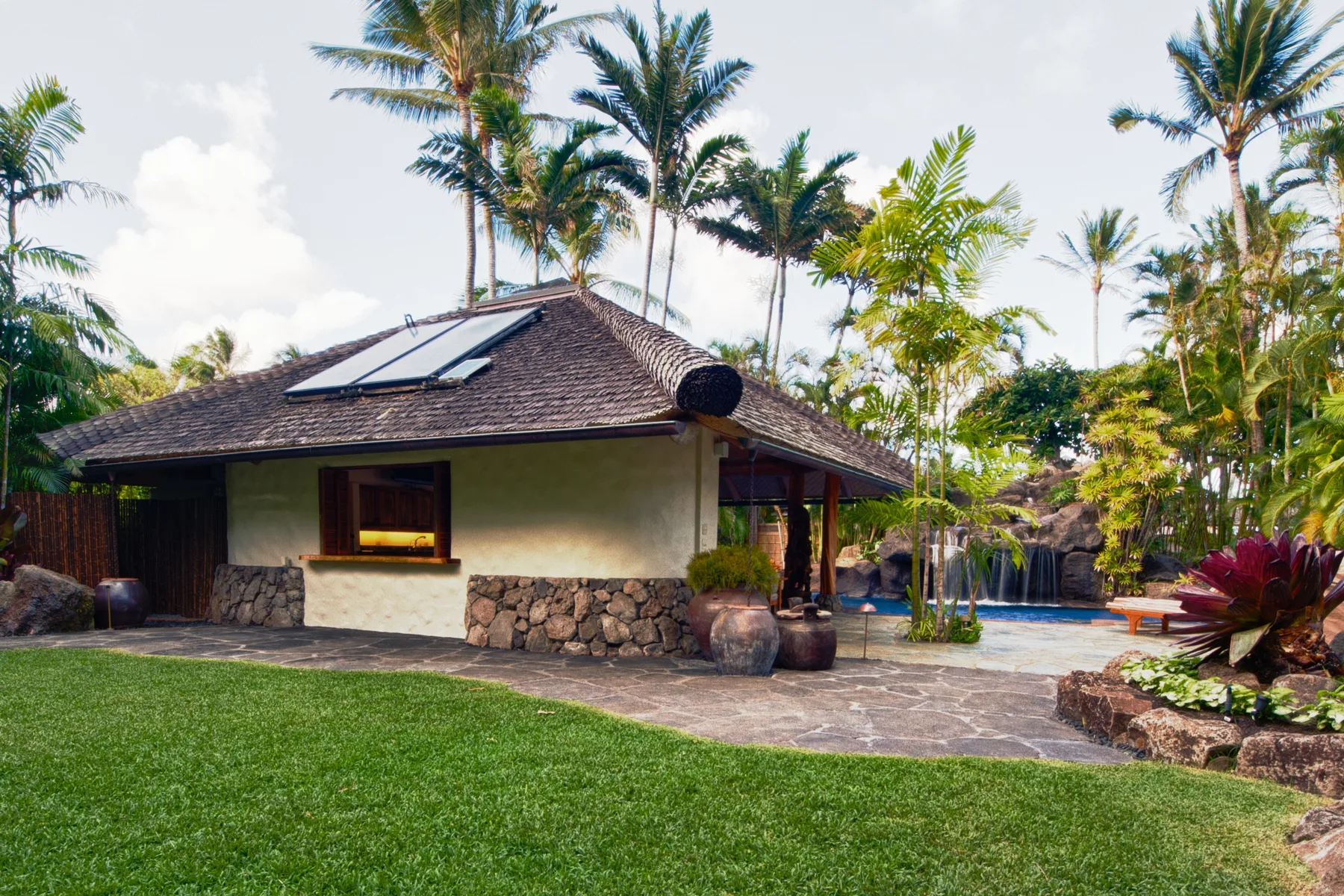Un edificio bajo de estilo tropical está junto a un patio pavimentado y una piscina.