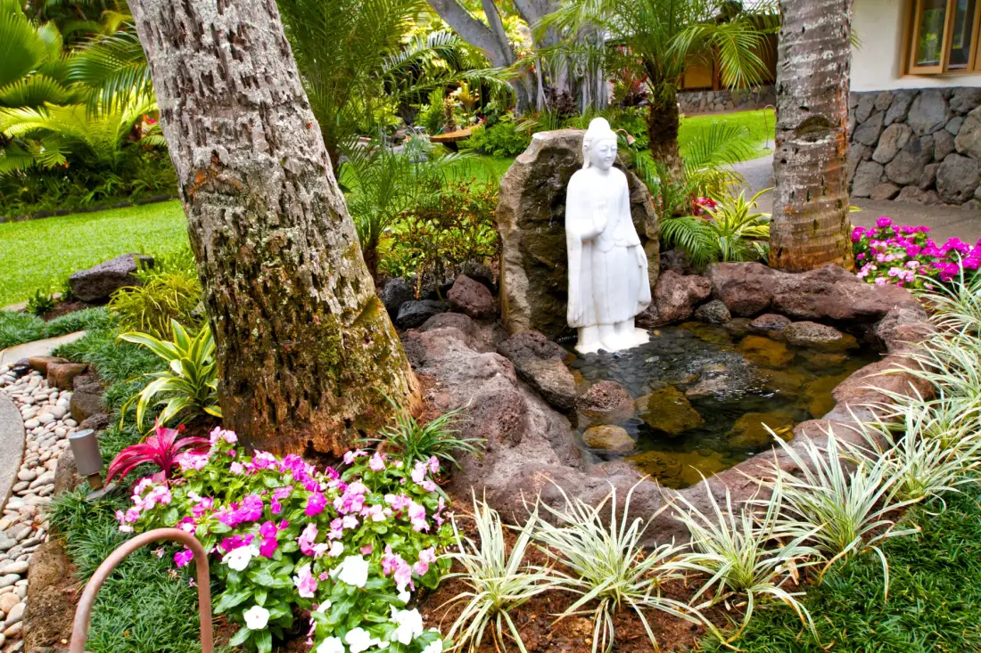 Un jardín tropical presenta una estatua blanca junto a un pequeño estanque.