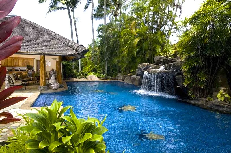Una piscina con una cascada junto a un pabellón abierto.