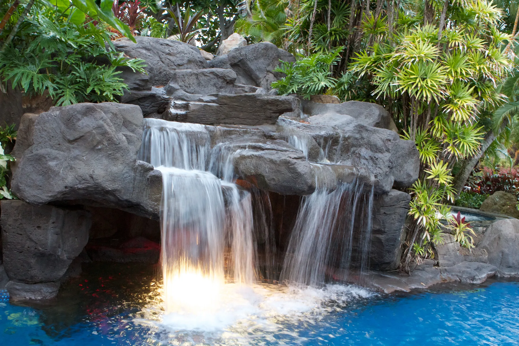 Una cascada cae sobre las rocas hacia una piscina azul rodeada de plantas tropicales.