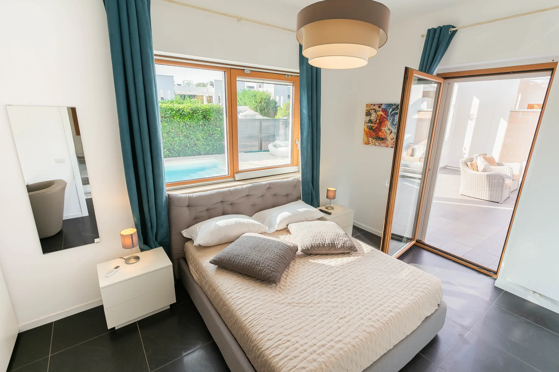 Un dormitorio con una cama bien arreglada junto a ventanas y cortinas verde azulado.