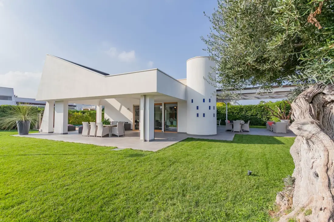 Una casa moderna se abre a un césped, con comedor y asientos al aire libre bajo un patio cubierto.