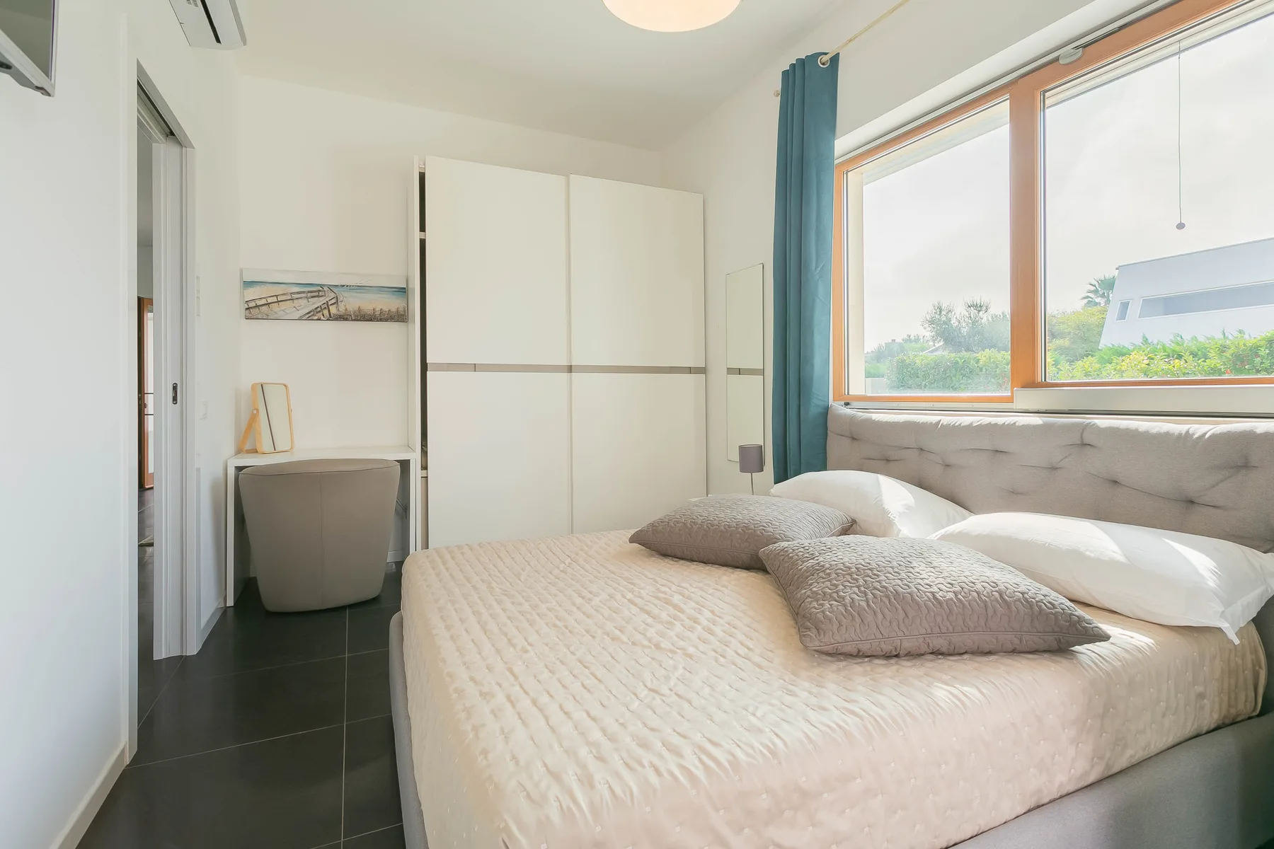 Un dormitorio con una cama junto a una ventana grande y cortinas verde azulado.