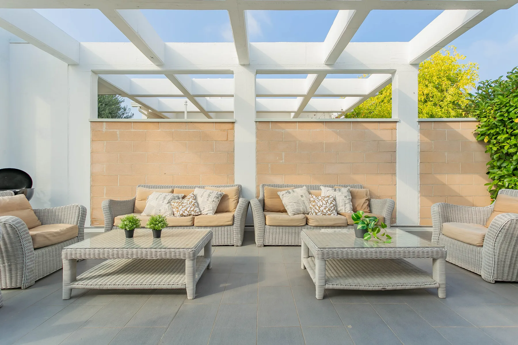 Una luminosa zona de estar al aire libre con muebles de mimbre bajo una pérgola blanca.