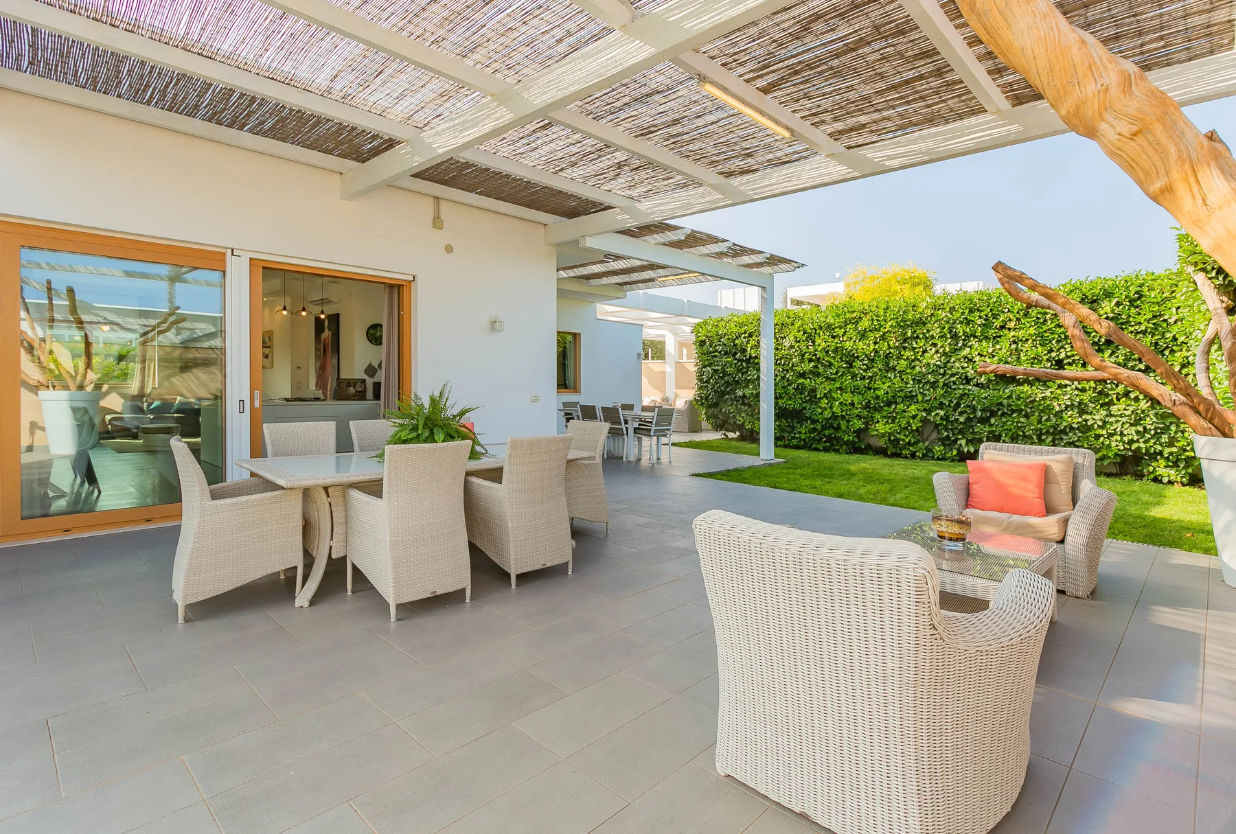 Un patio cubierto con asientos de mimbre y una mesa de comedor da a un jardín verde.