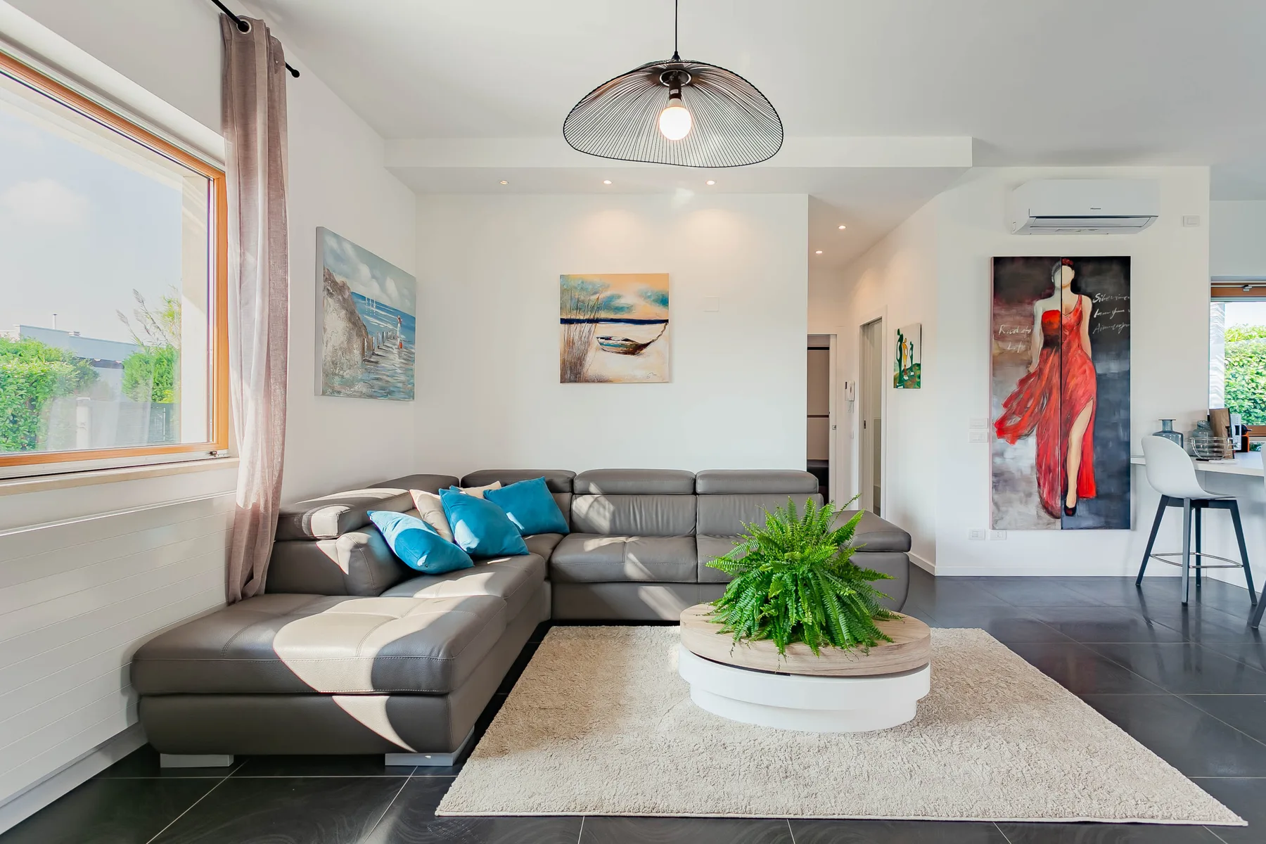 Una sala luminosa con asientos grises, cojines de colores y una planta en maceta.