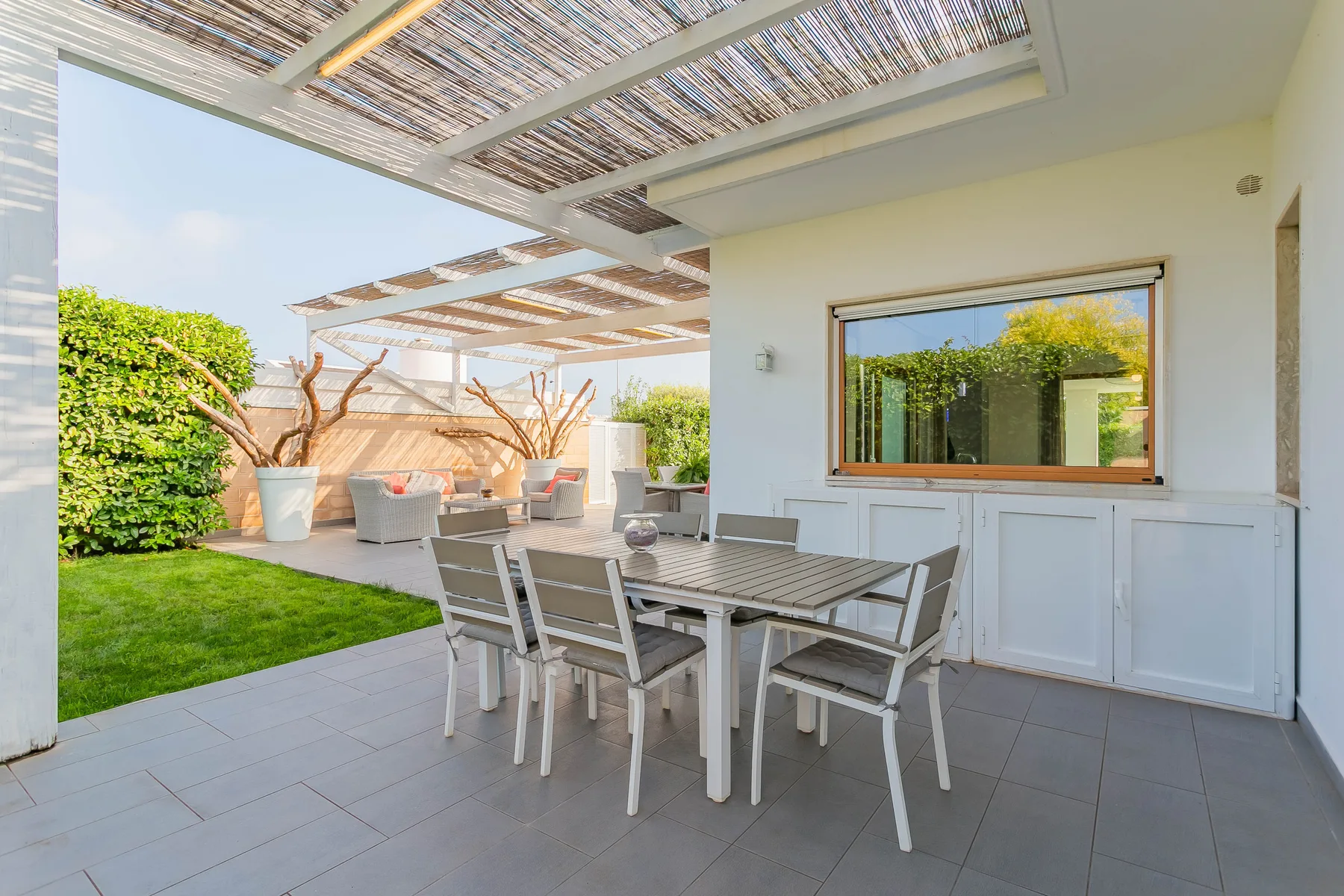 Comedor exterior cubierto con una mesa y asientos junto a un pequeño césped.