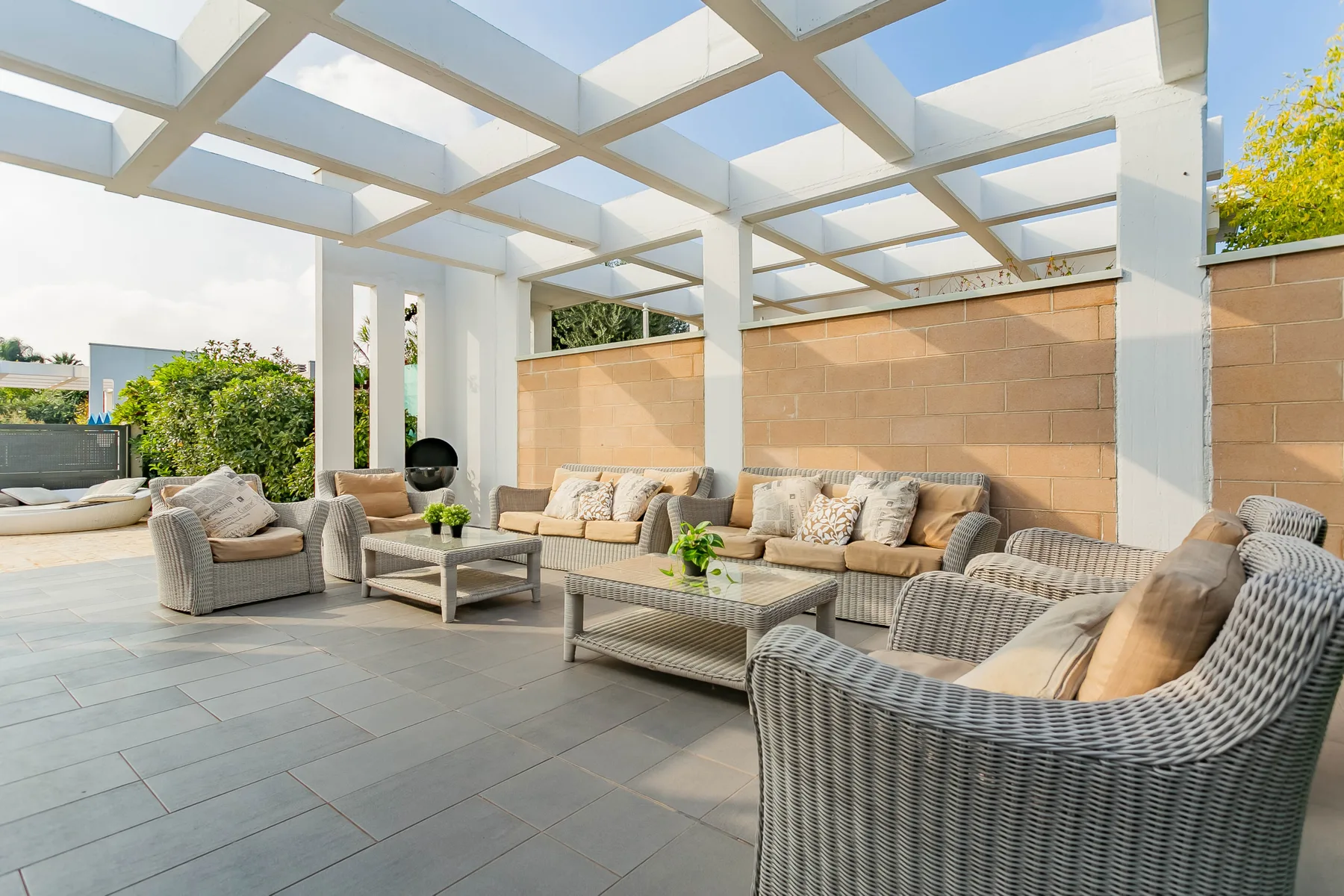 Una zona de estar al aire libre bajo una pérgola blanca, con una mesa baja.
