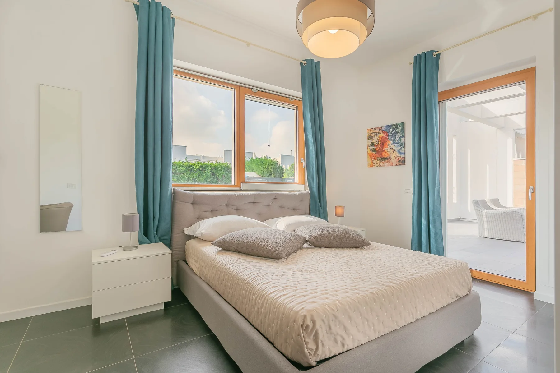 Un dormitorio con una cama doble bajo una ventana, enmarcada por cortinas verde azulado.