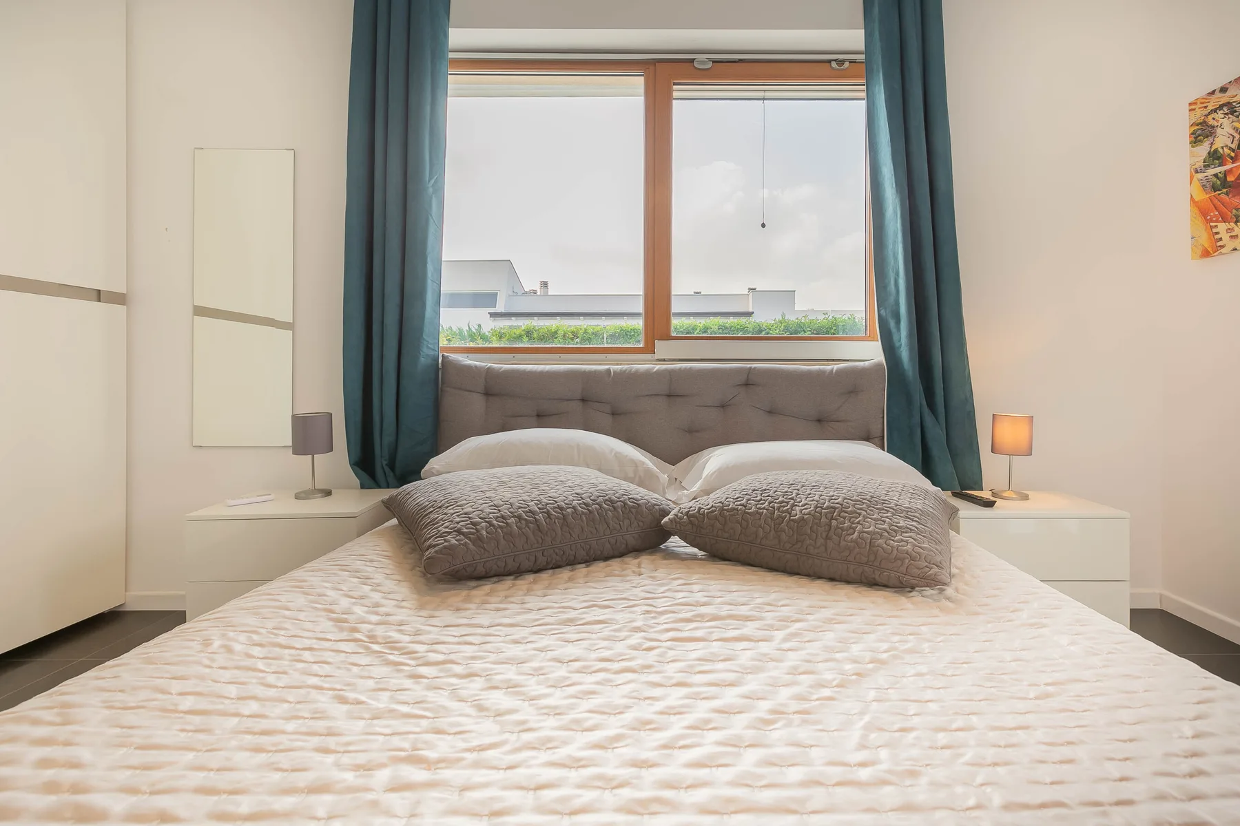 Un dormitorio con una cama bajo una ventana enmarcada por cortinas verde azulado.