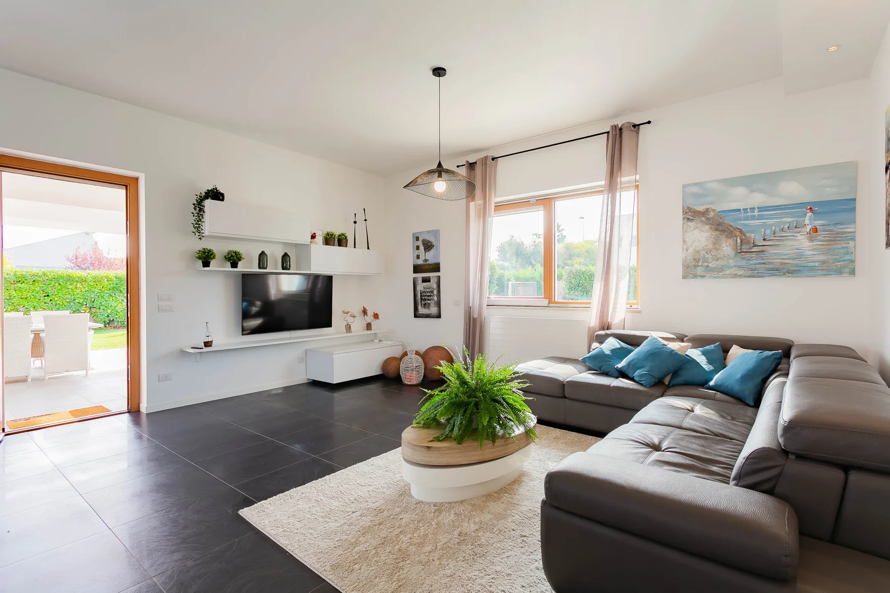 Una sala luminosa con zona de asientos, televisor y una planta en maceta.