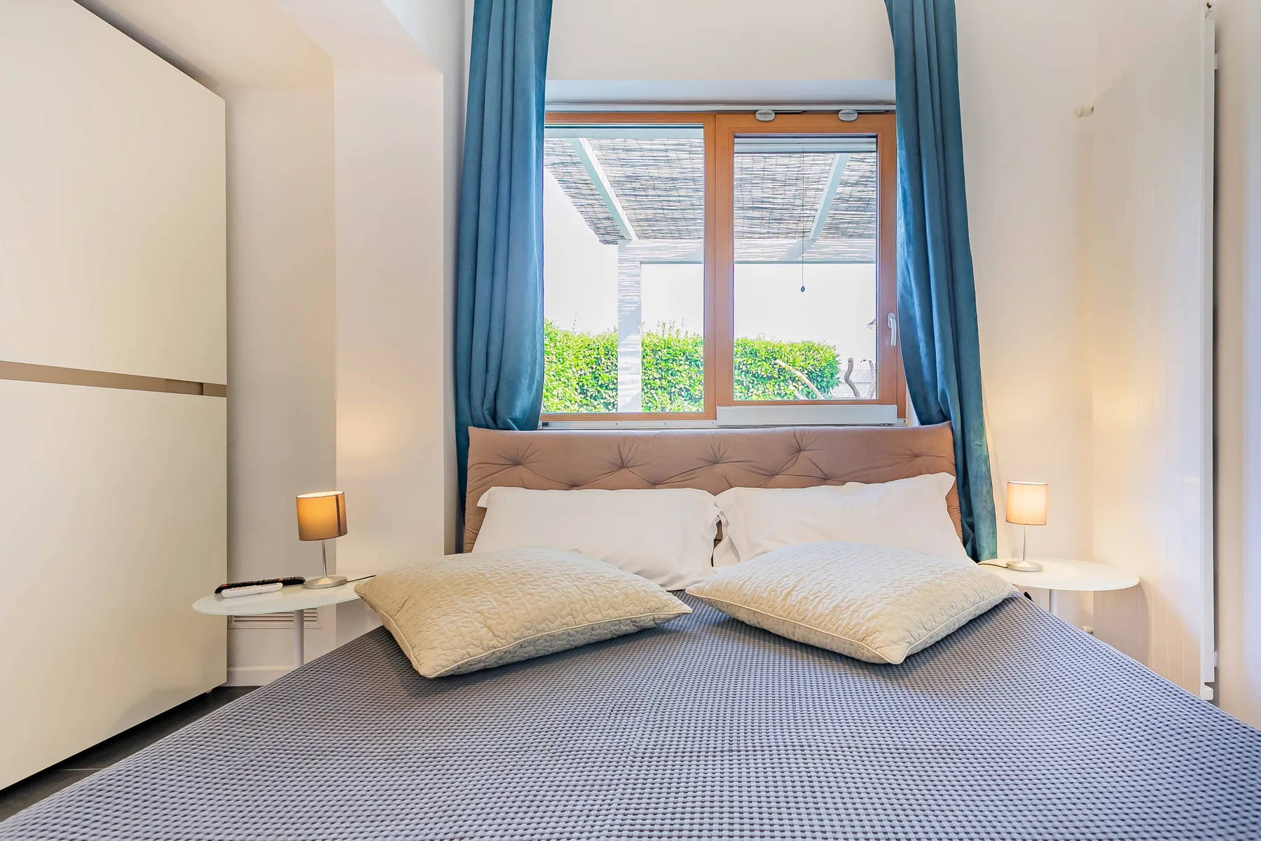 Un dormitorio con una cama bien hecha bajo una ventana enmarcada por cortinas azules.