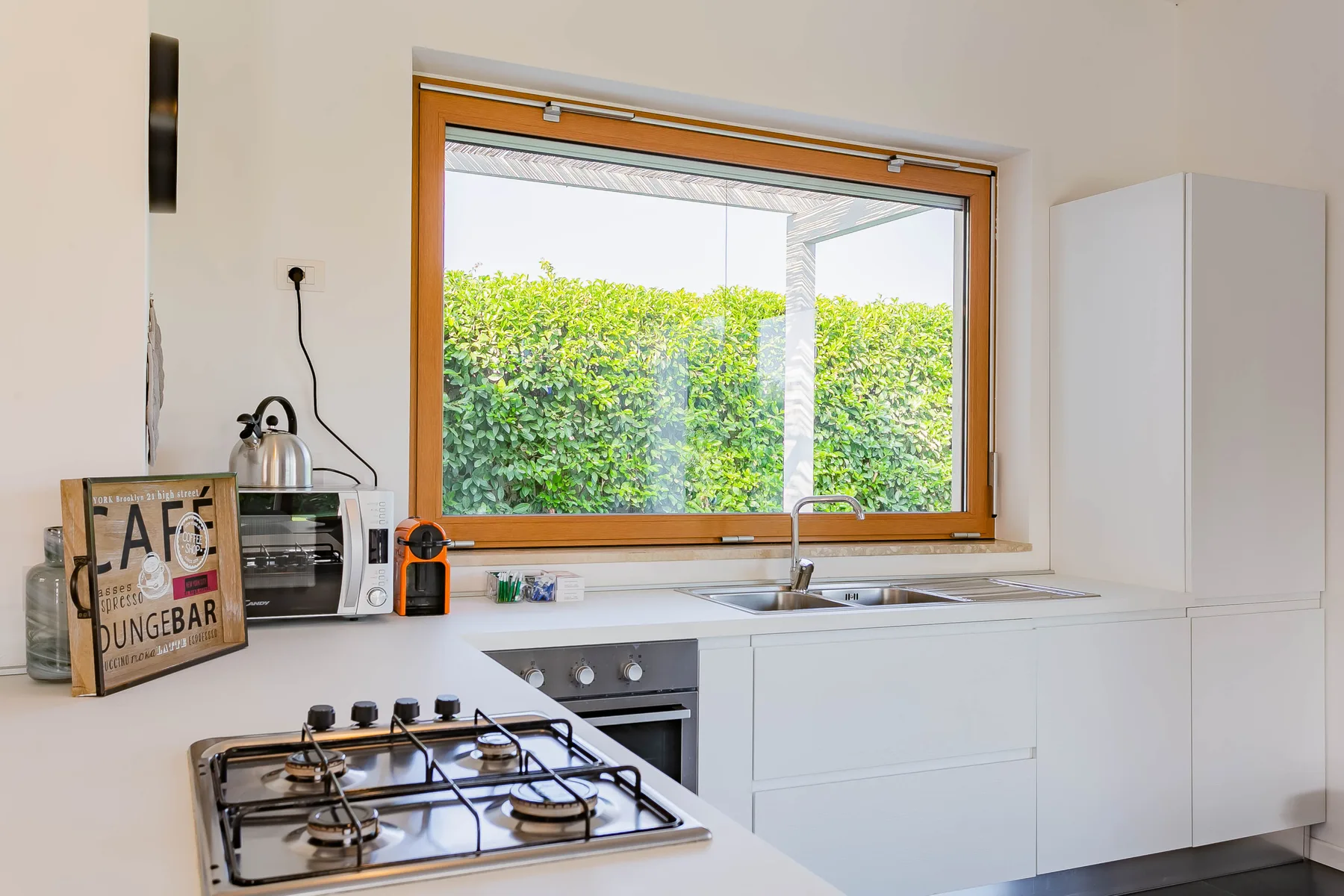 Una cocina luminosa con una estufa y un fregadero bajo una ventana grande.