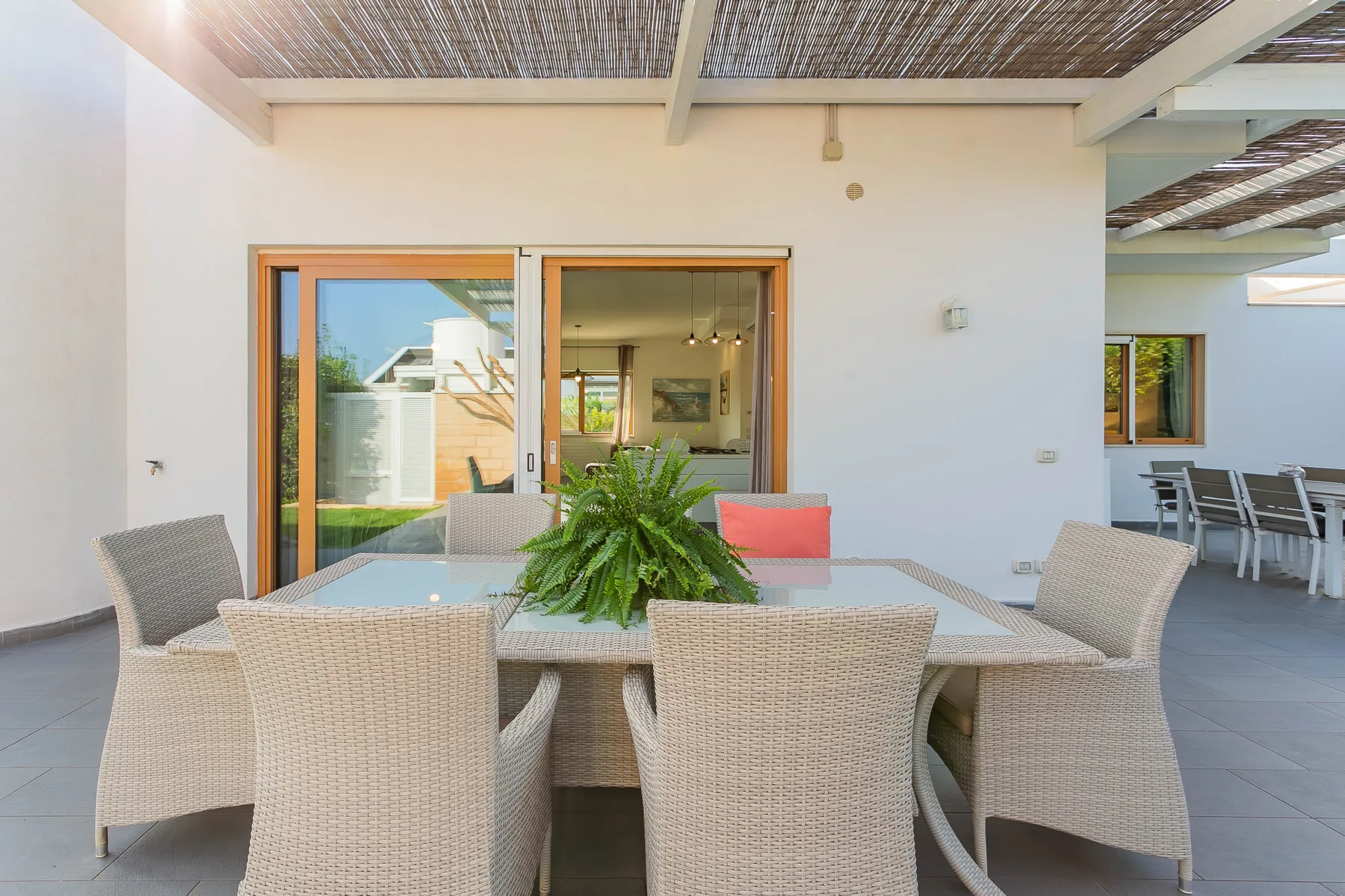 Comedor exterior cubierto con una mesa, asientos y plantas en maceta.
