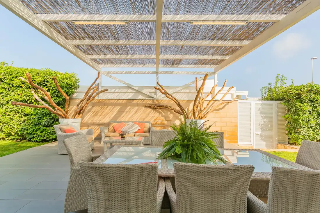 Un patio al aire libre con asientos tejidos bajo una pérgola de listones.