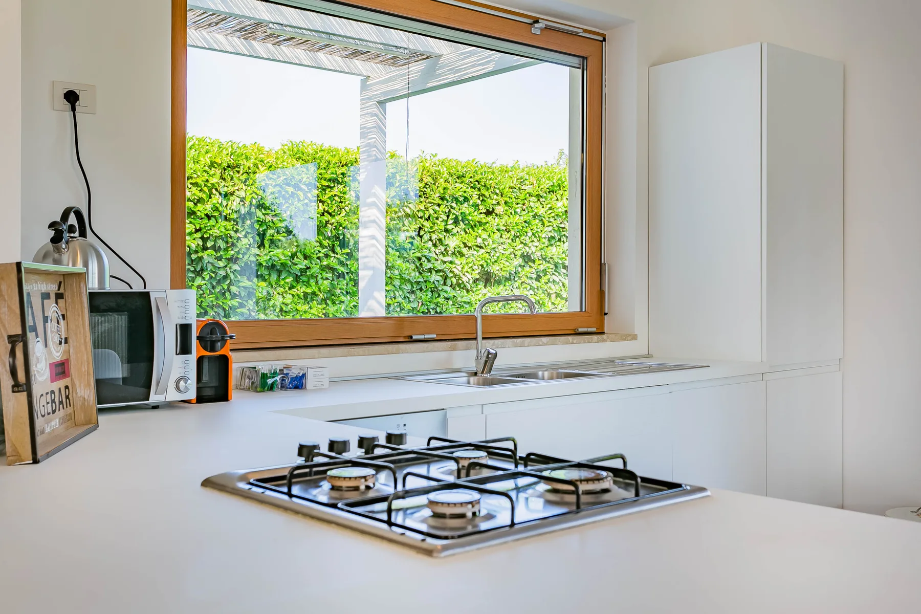 Una cocina luminosa con cocina de gas, fregadero y una ventana grande con vista a la vegetación.