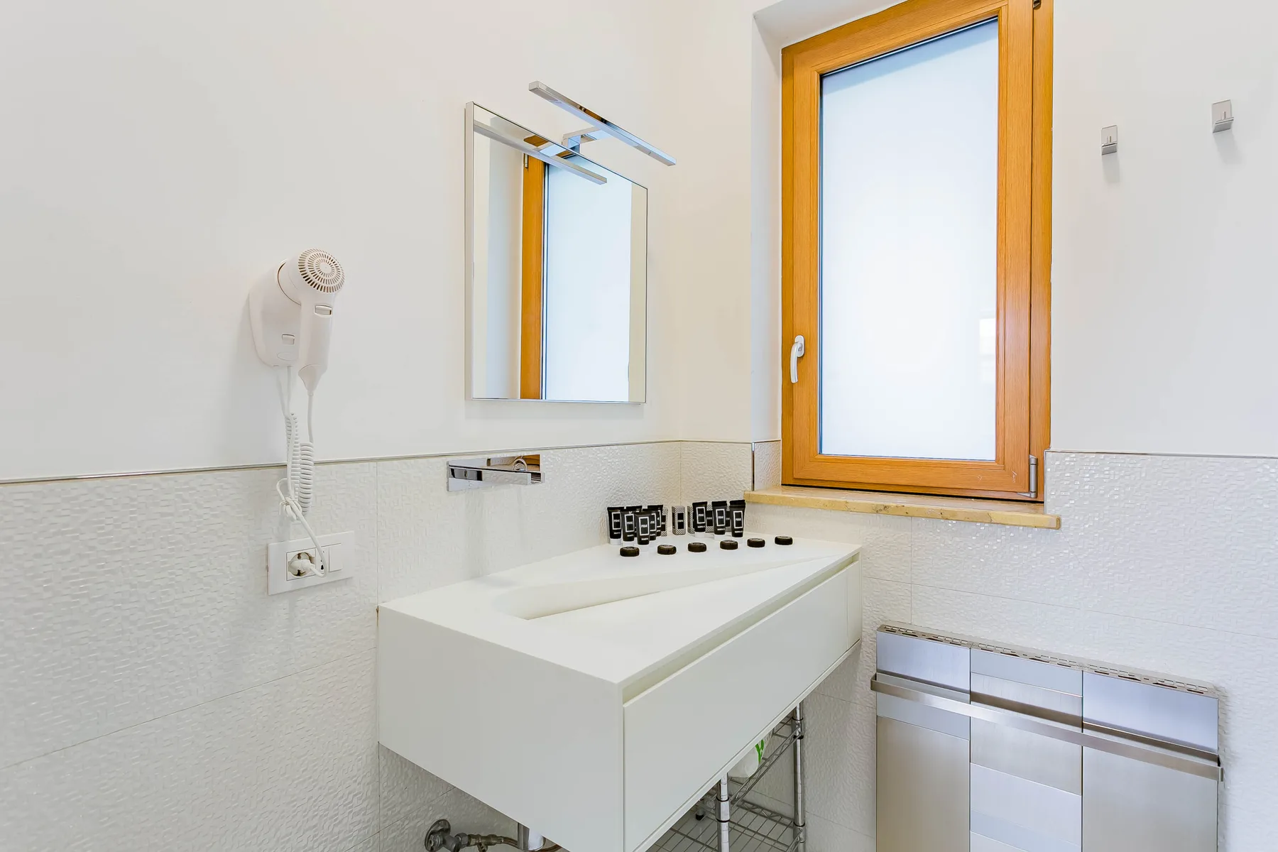 Un baño luminoso con un espejo de pared sobre un lavabo blanco.