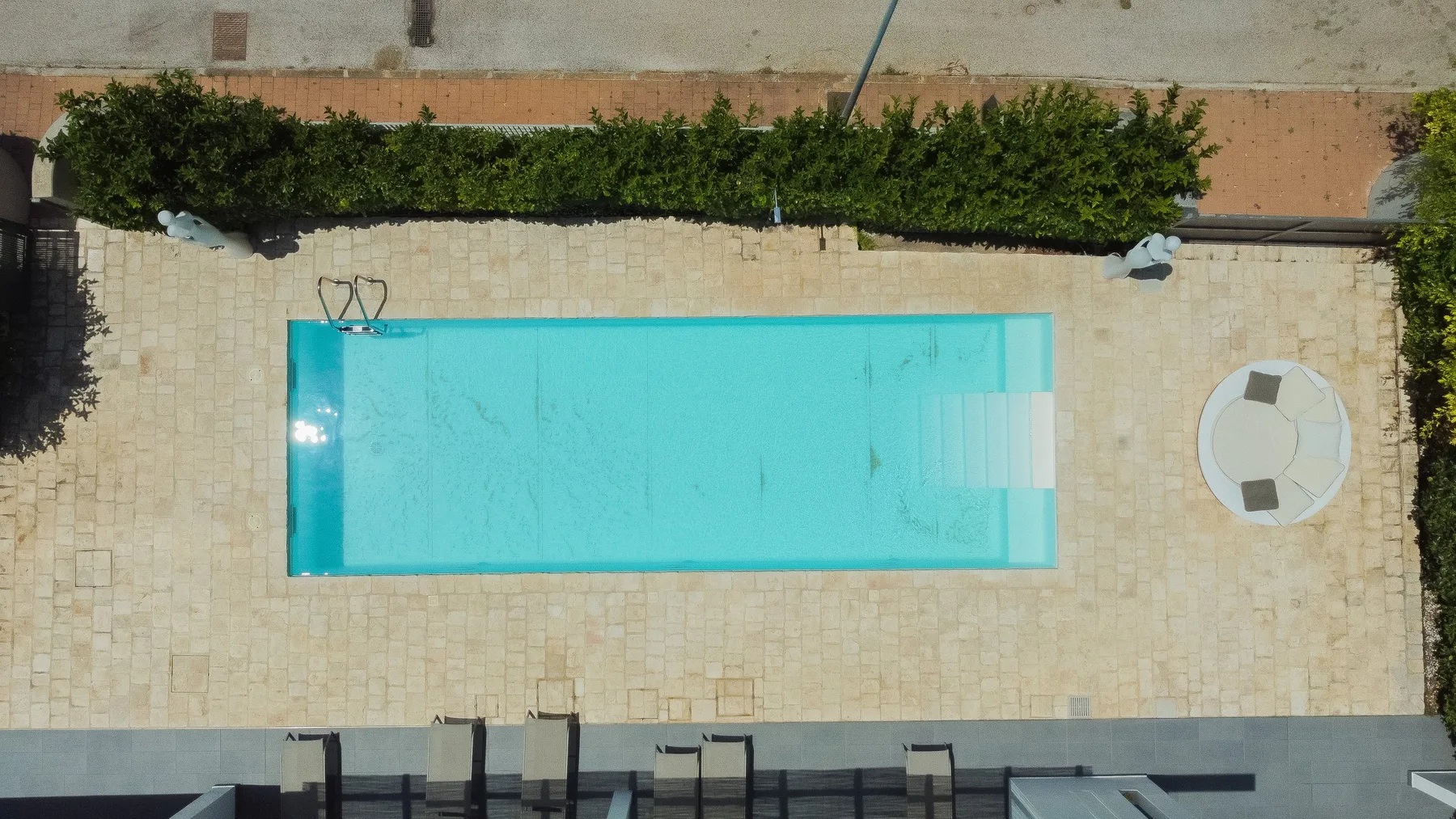 Vista desde arriba de una piscina rectangular rodeada por un patio pavimentado.