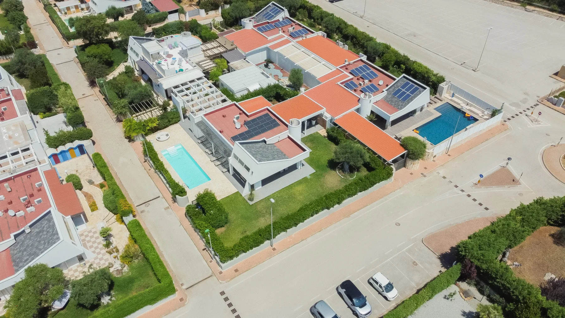 Vista aérea de un complejo moderno con tejados naranjas, una piscina y zonas exteriores.