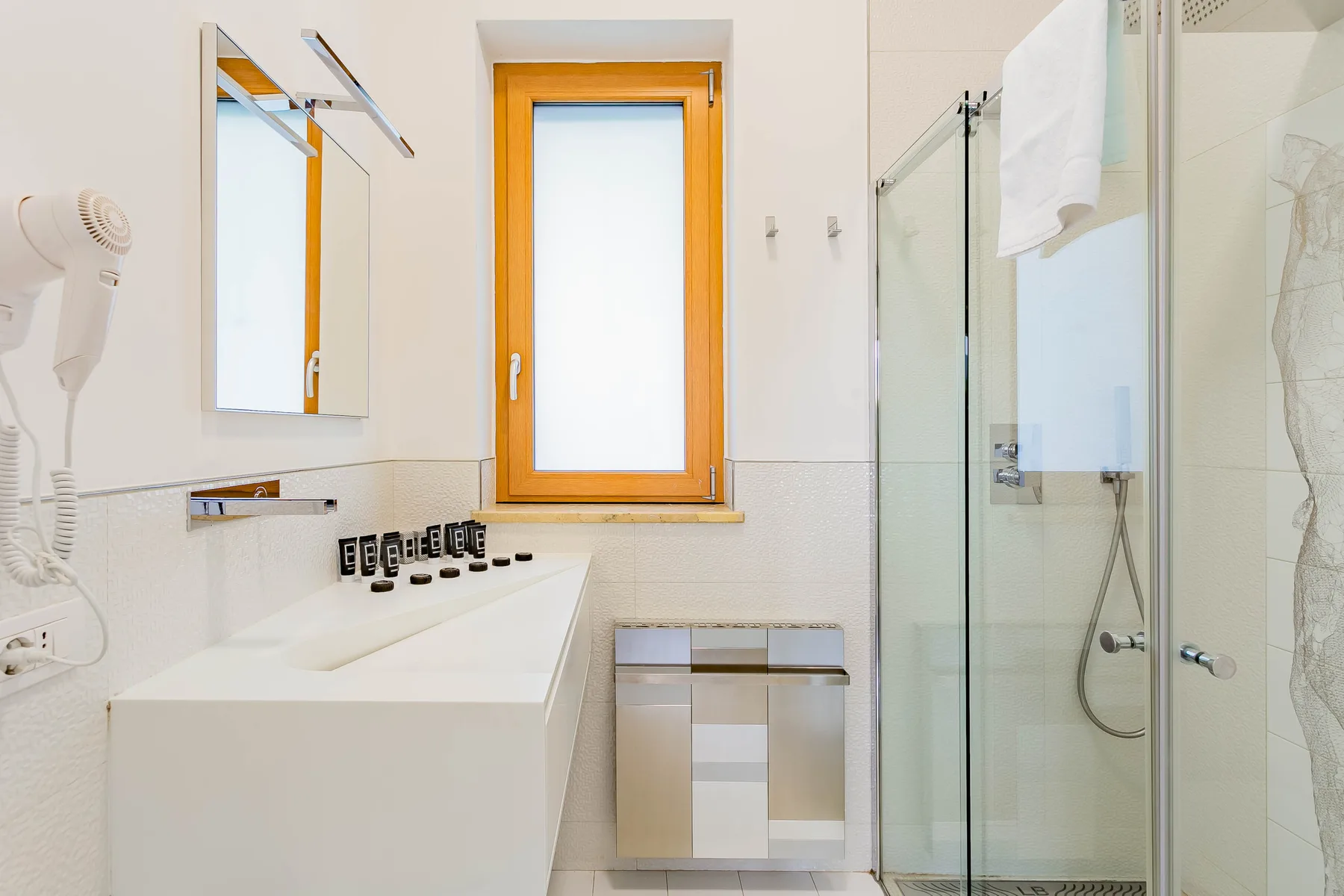 Un baño luminoso con lavabo, ventana y ducha de vidrio.