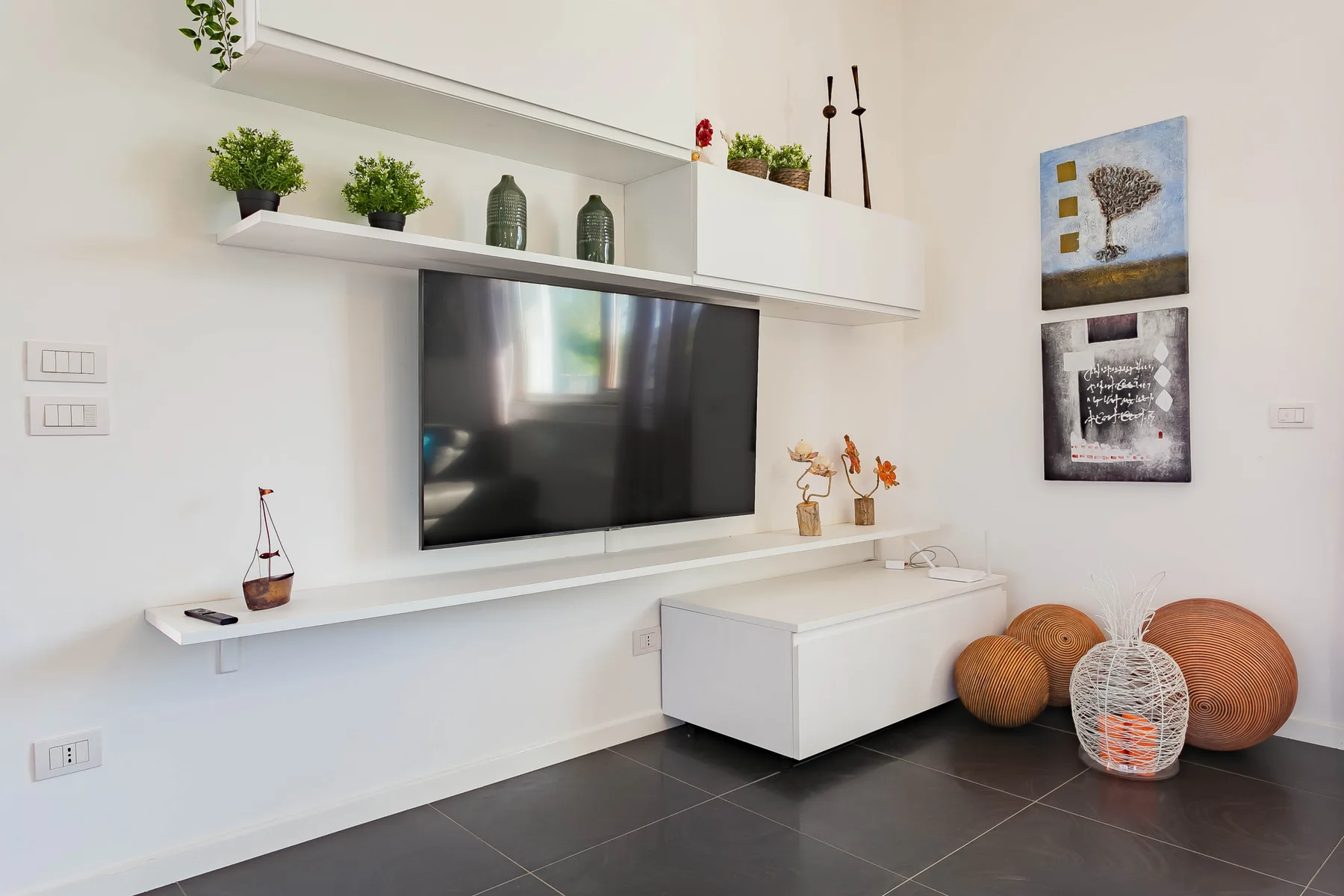 Una sala de estar con televisor en la pared, estantes flotantes y asientos en el suelo.