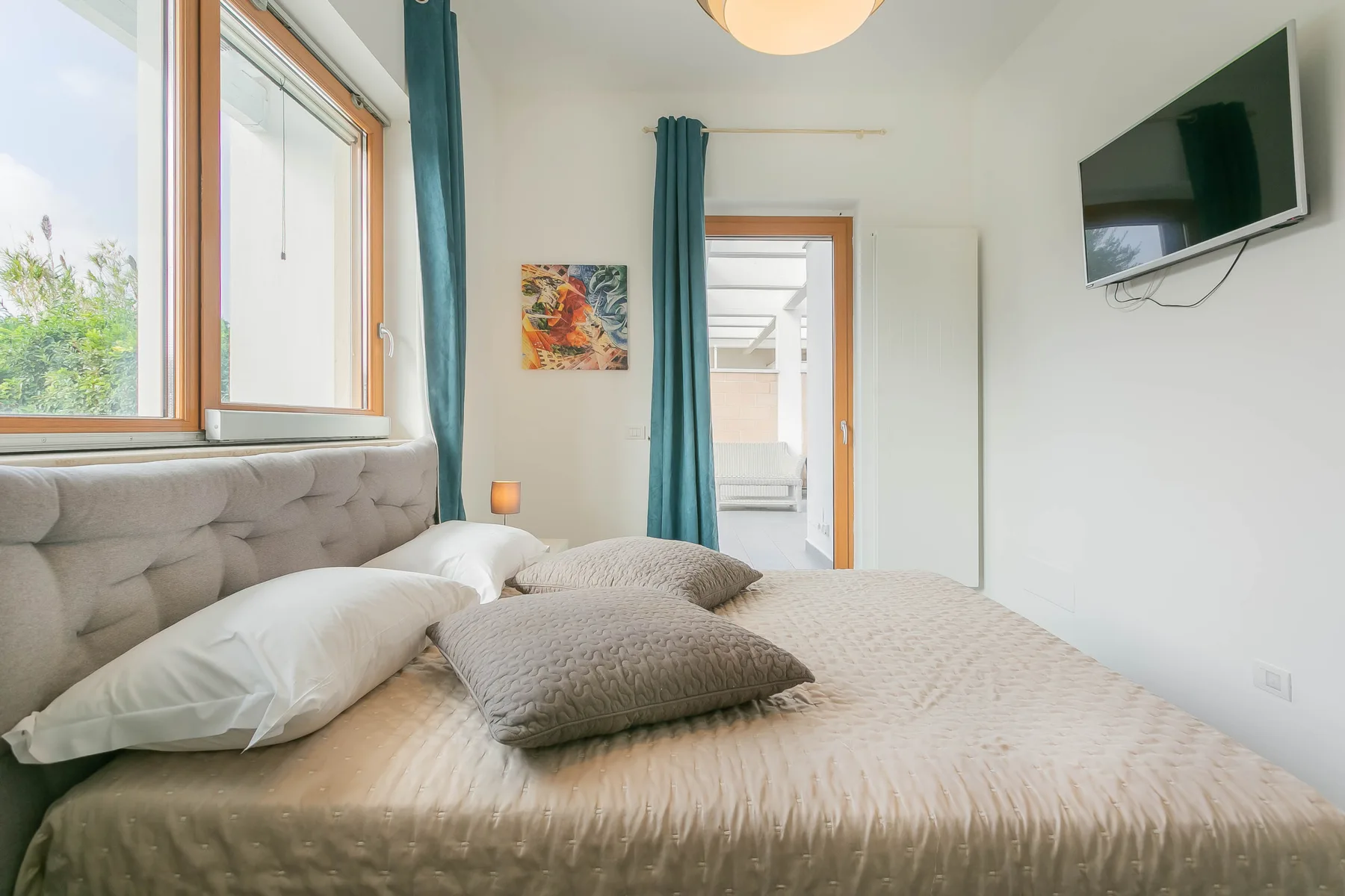Un dormitorio con una cama, cortinas color verde azulado y un televisor en la pared.