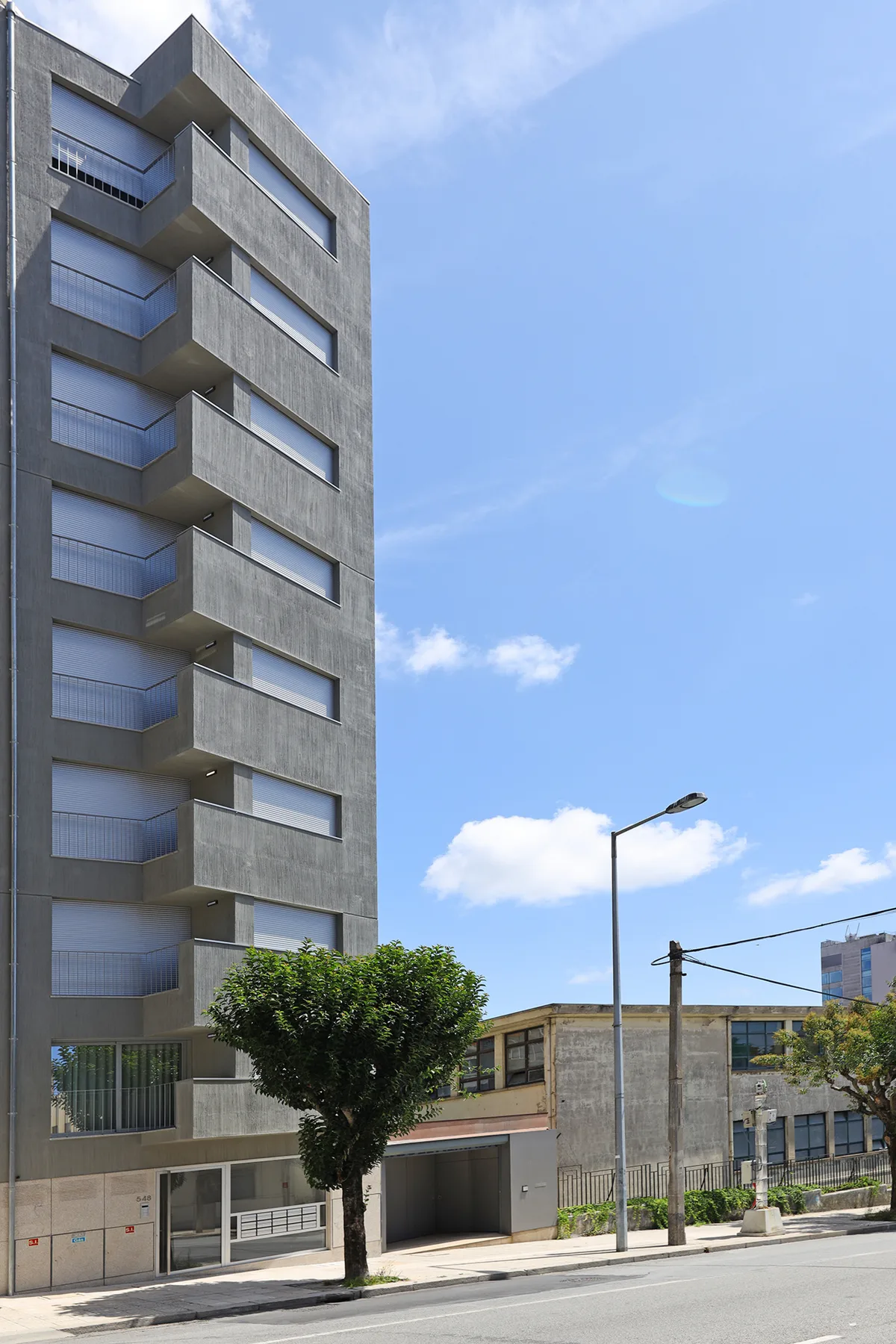 A modern apartment building stands beside a tree-lined street under a clear sky.