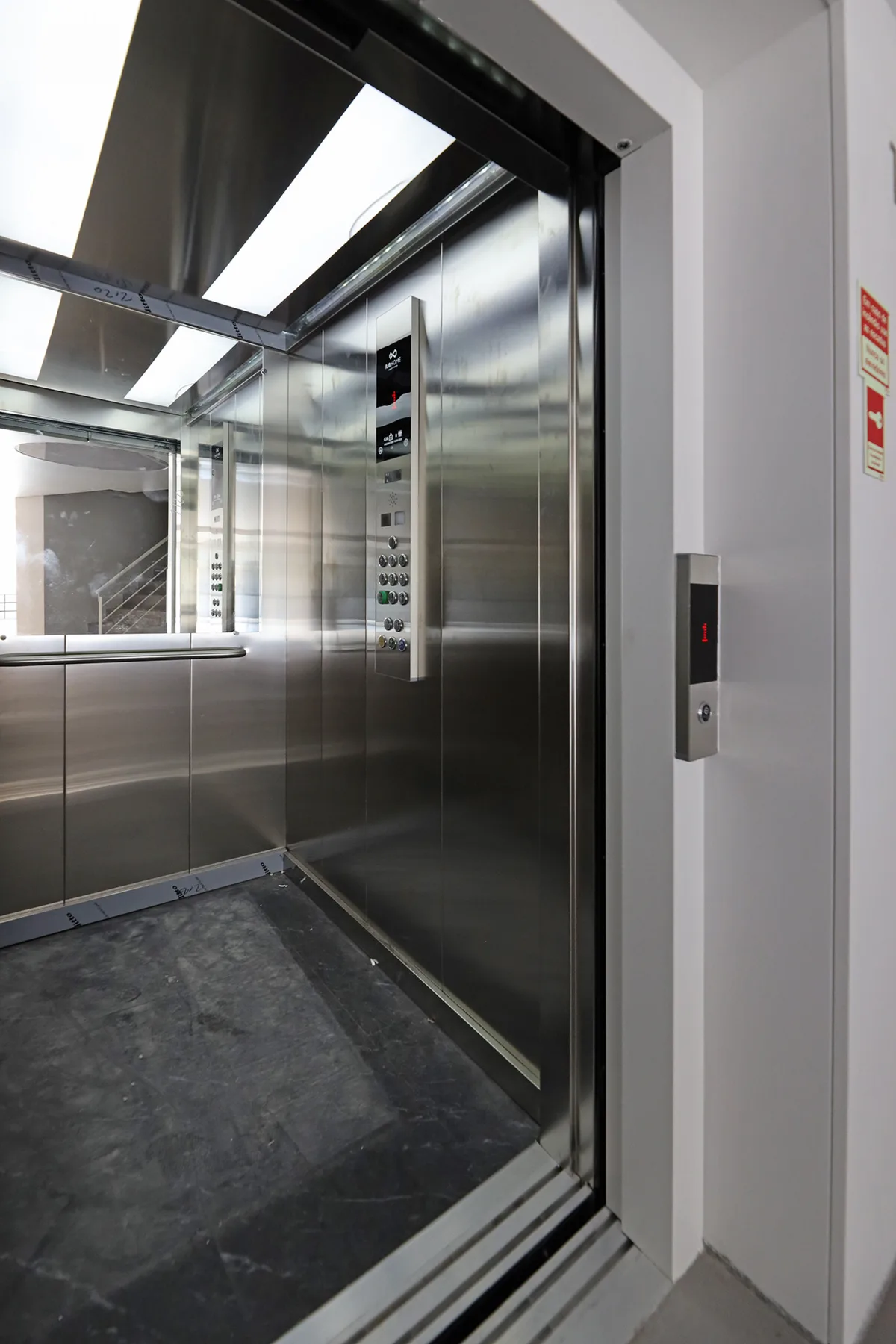 An open elevator with reflective metal walls and a dark floor.