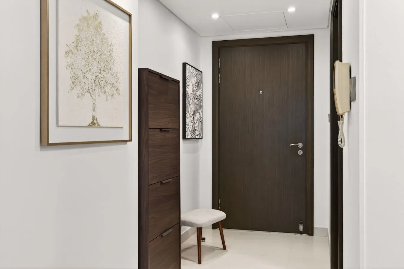 Un recibidor luminoso con una puerta de madera oscura y cuadros enmarcados.
