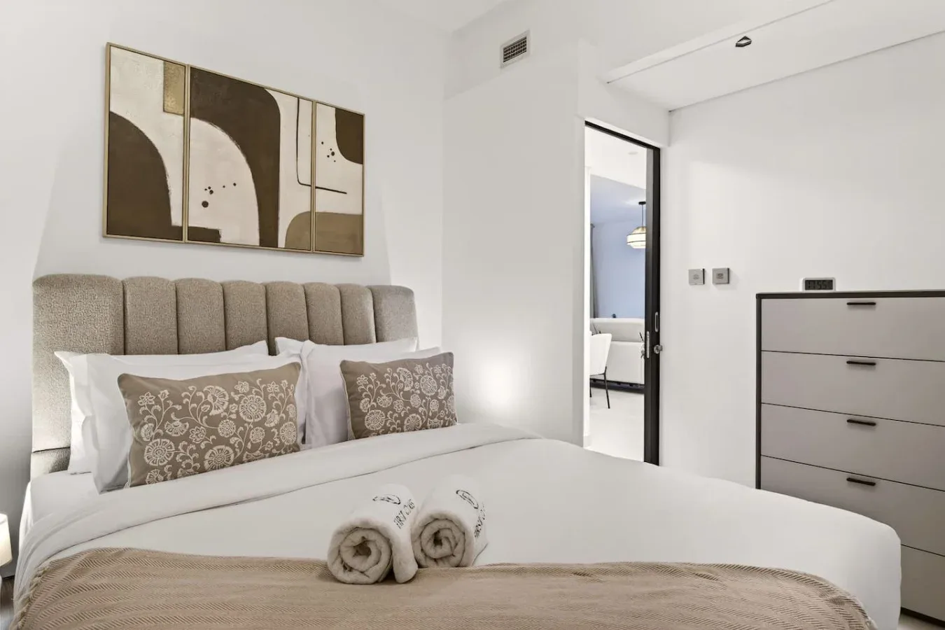 Un dormitorio luminoso con una cama tendida y arte abstracto en la pared.