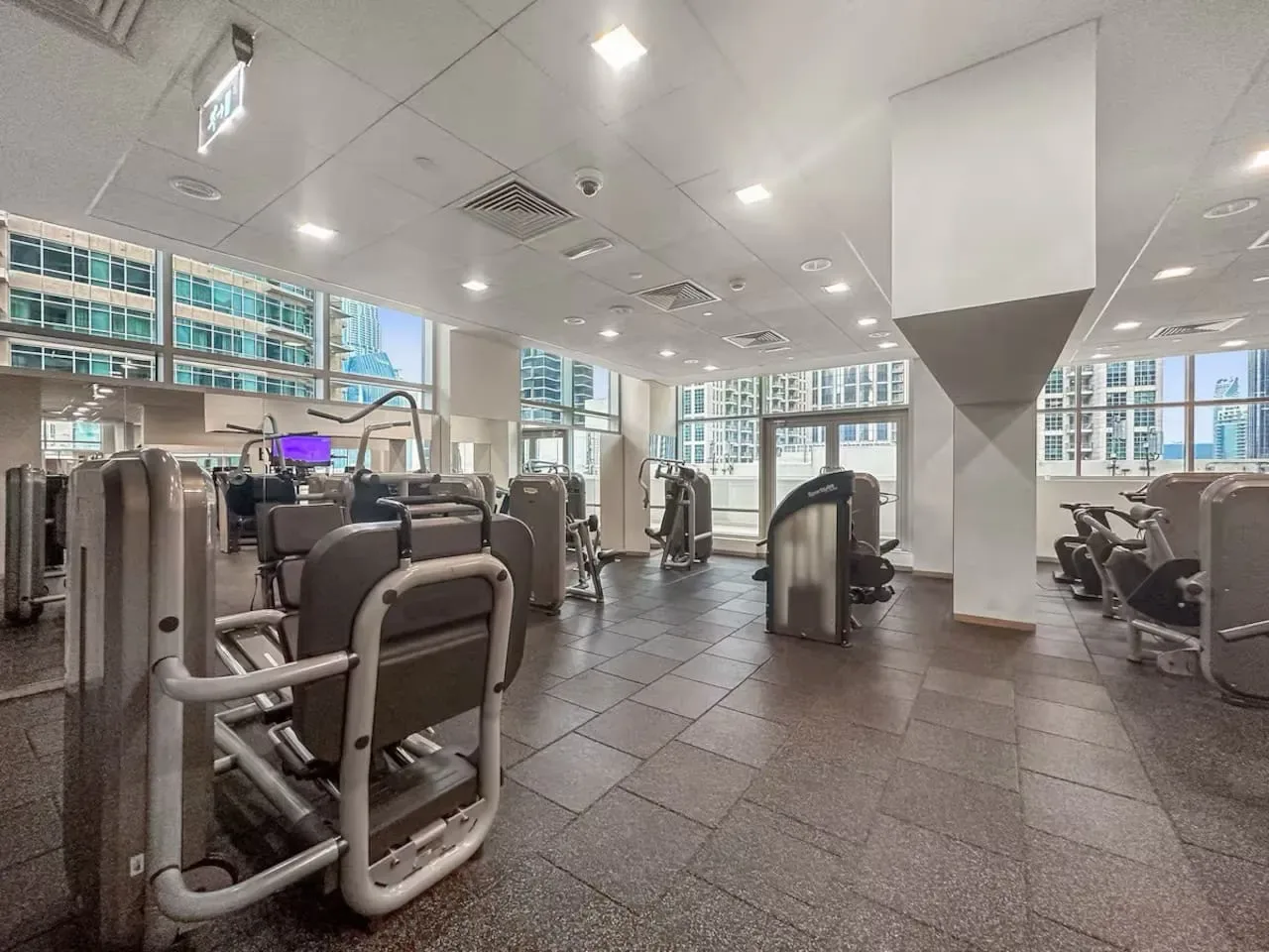 Un gimnasio con máquinas de ejercicio junto a grandes ventanales.