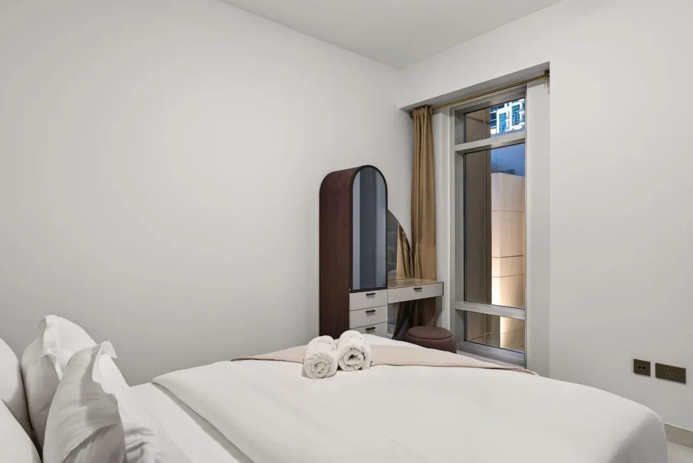 Un dormitorio con una cama arreglada, un tocador y una ventana.