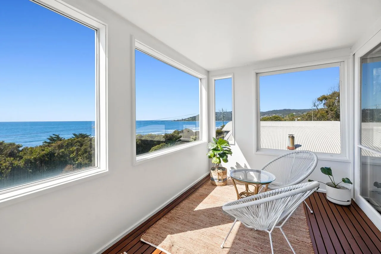 A bright sunroom with large windows overlooking the ocean and a seating area.