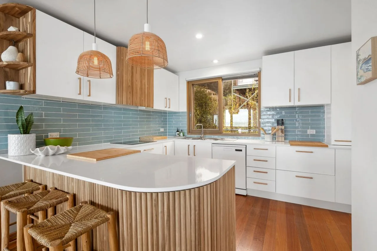 A bright kitchen with a curved island, pendant lights, and blue tile backsplash.
