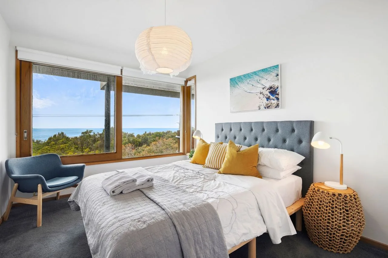 A bedroom with a large bed beside windows overlooking the ocean.
