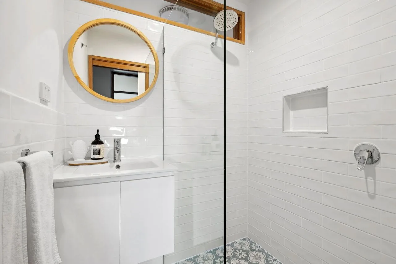 A bright bathroom with a vanity, round mirror, and glass shower.