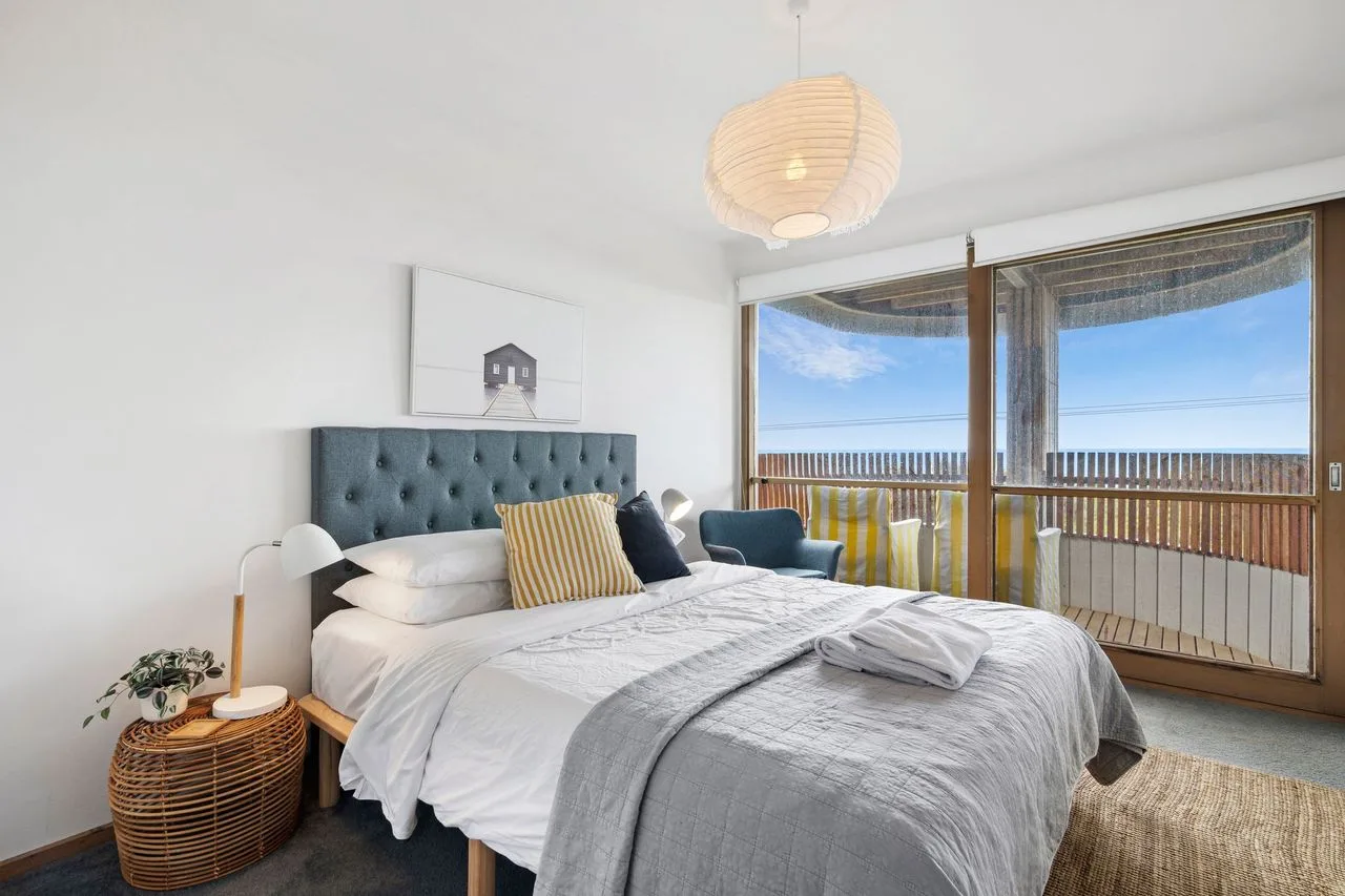 A bright bedroom with a large bed and windows opening onto a balcony.