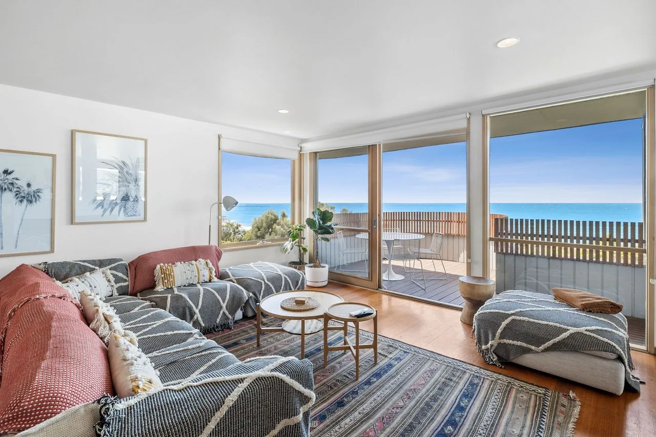 A living room with seating and large windows overlooking the ocean.