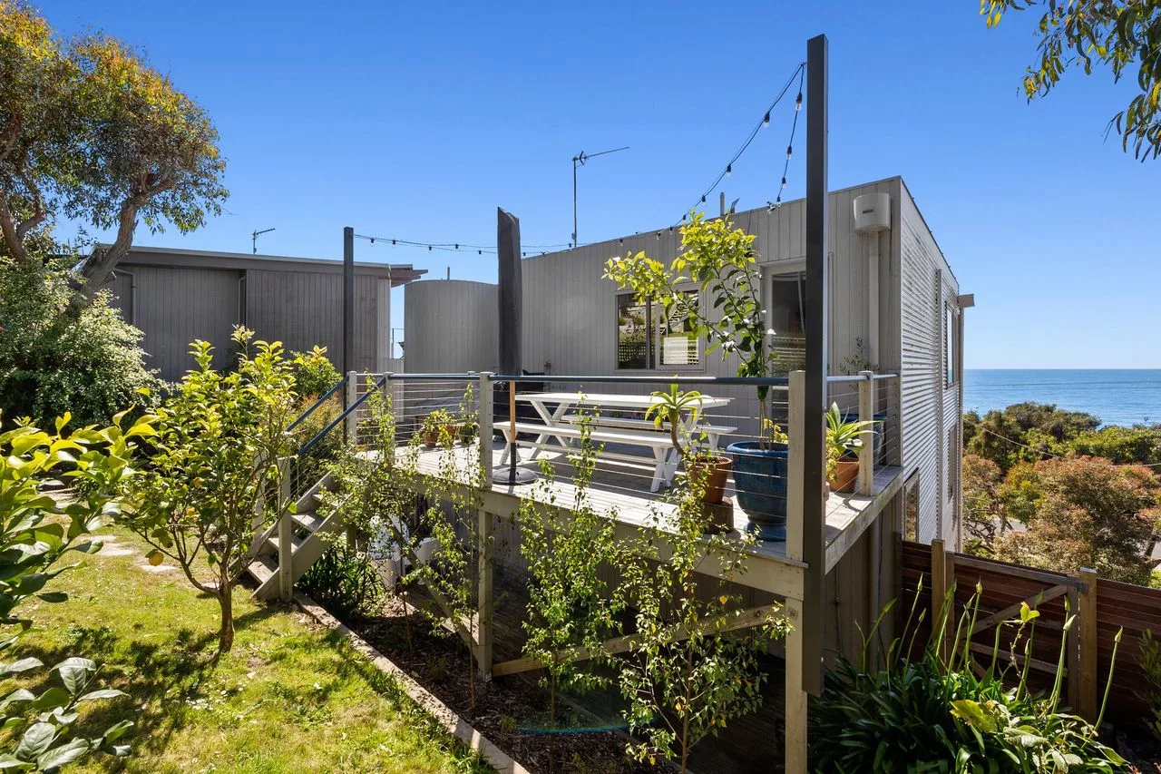 A raised outdoor deck with seating overlooks coastal vegetation and the ocean.