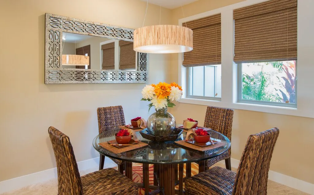 A dining area with a round glass table, woven seating, and flowers.