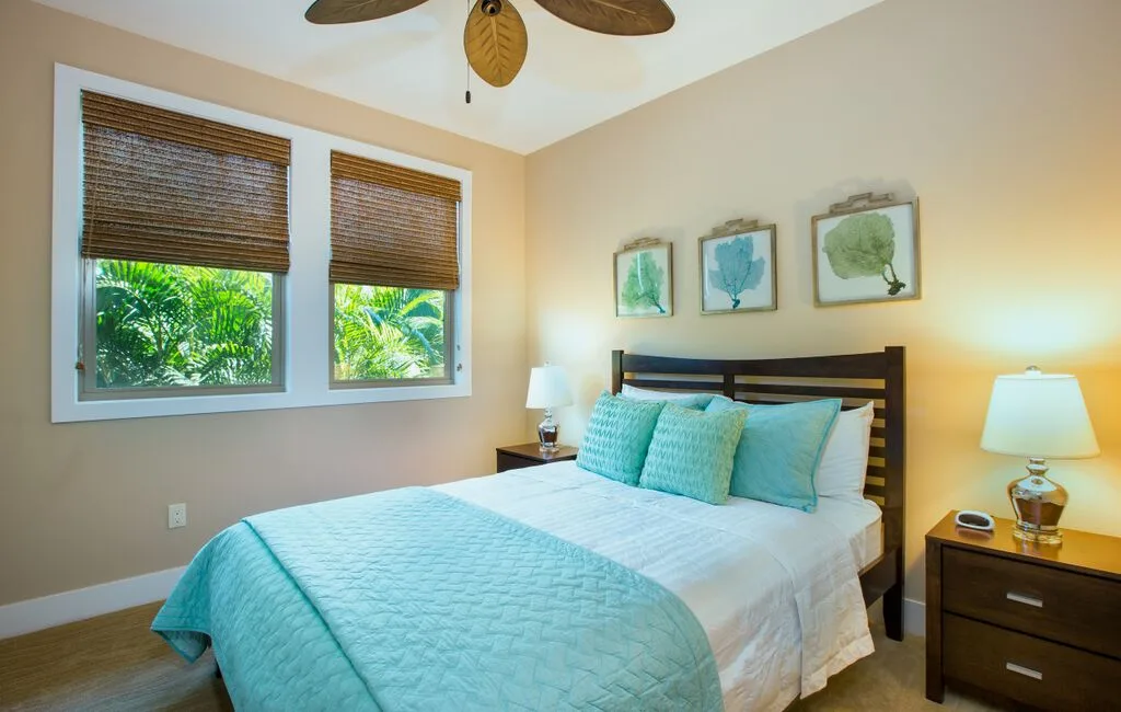 A bedroom with a bed dressed in turquoise bedding beneath three framed botanical prints.