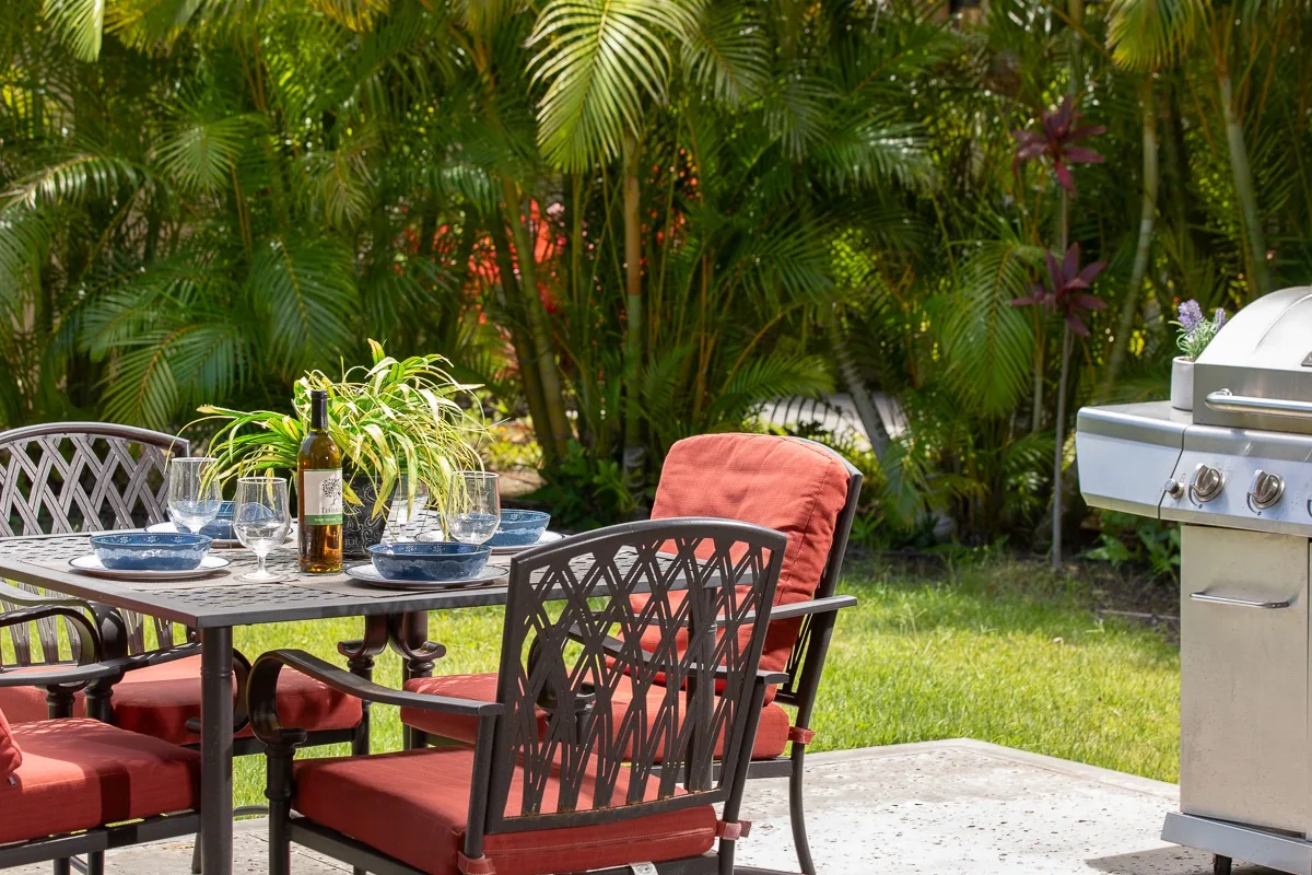 An outdoor patio dining area with red-cushioned seating beside a grill.